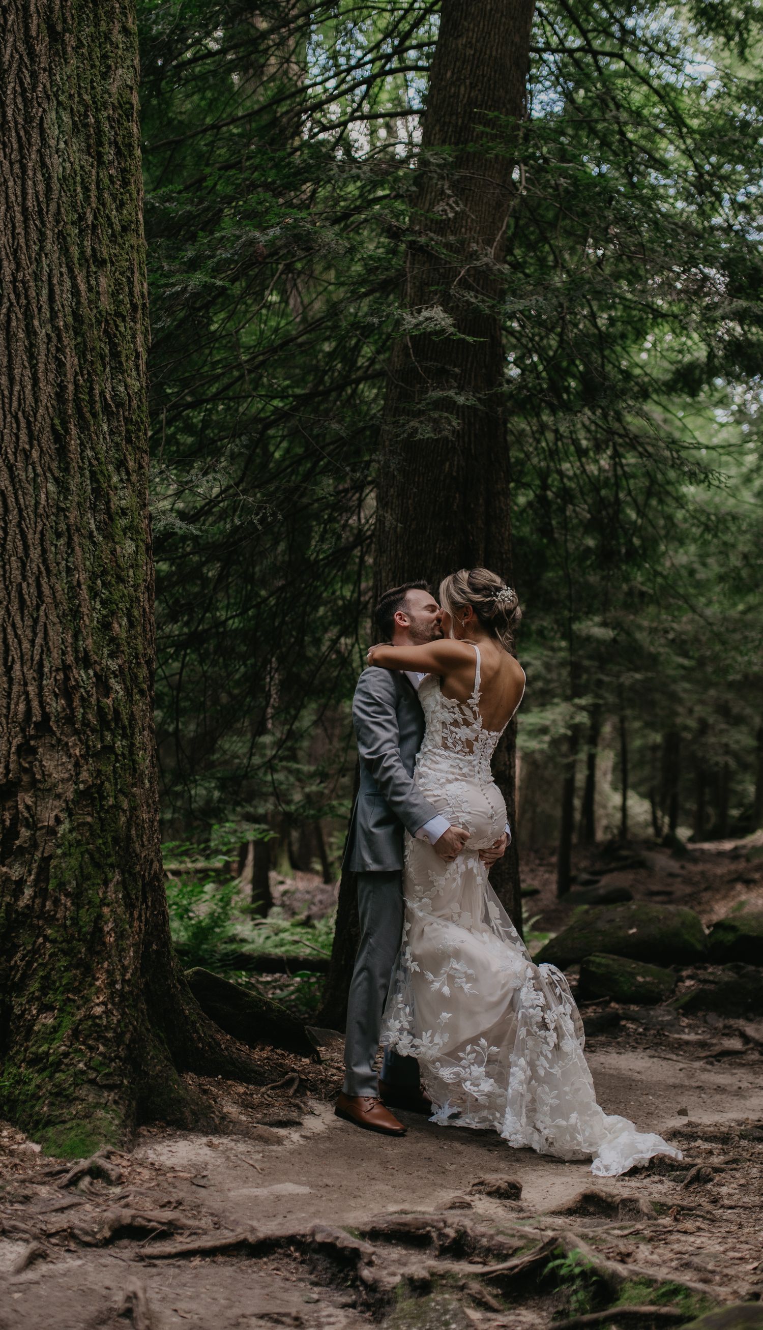 Wedding couple embraces among tall pine trees on a forest path.
