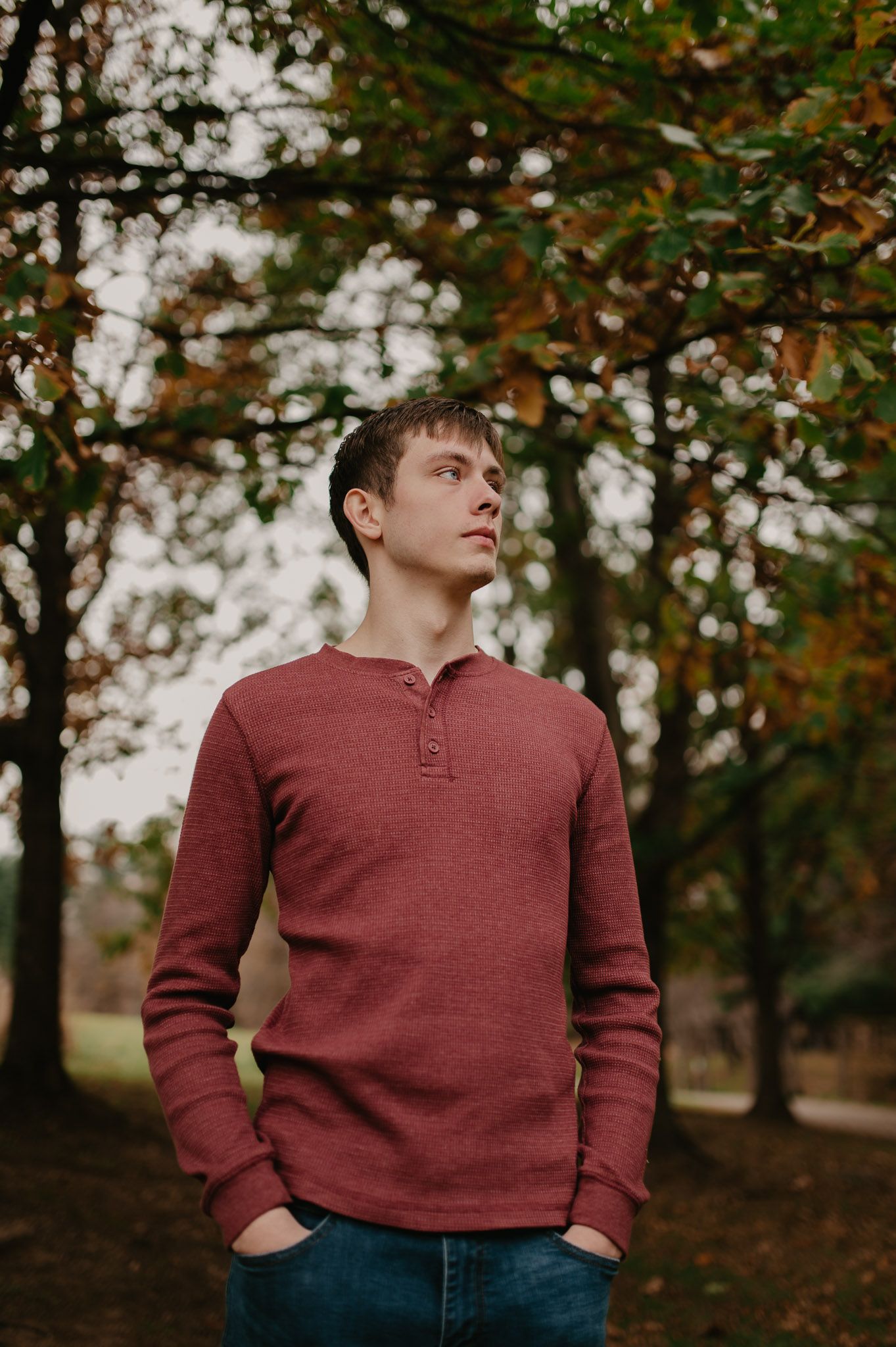Person in red henley sweater posing against autumn forest background.