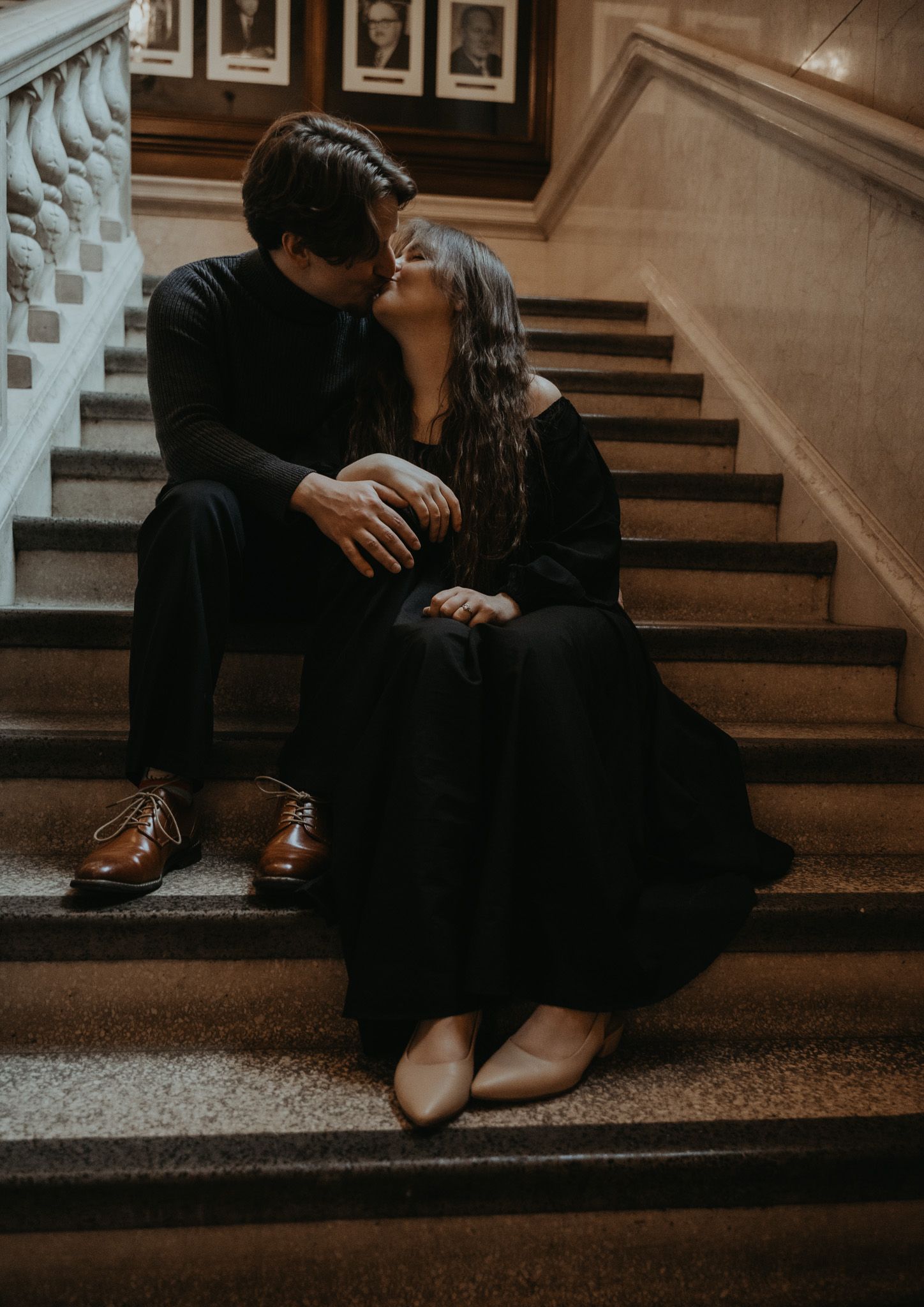 A romantic couple in dark clothing share an intimate moment while sitting on vintage wooden stairs.