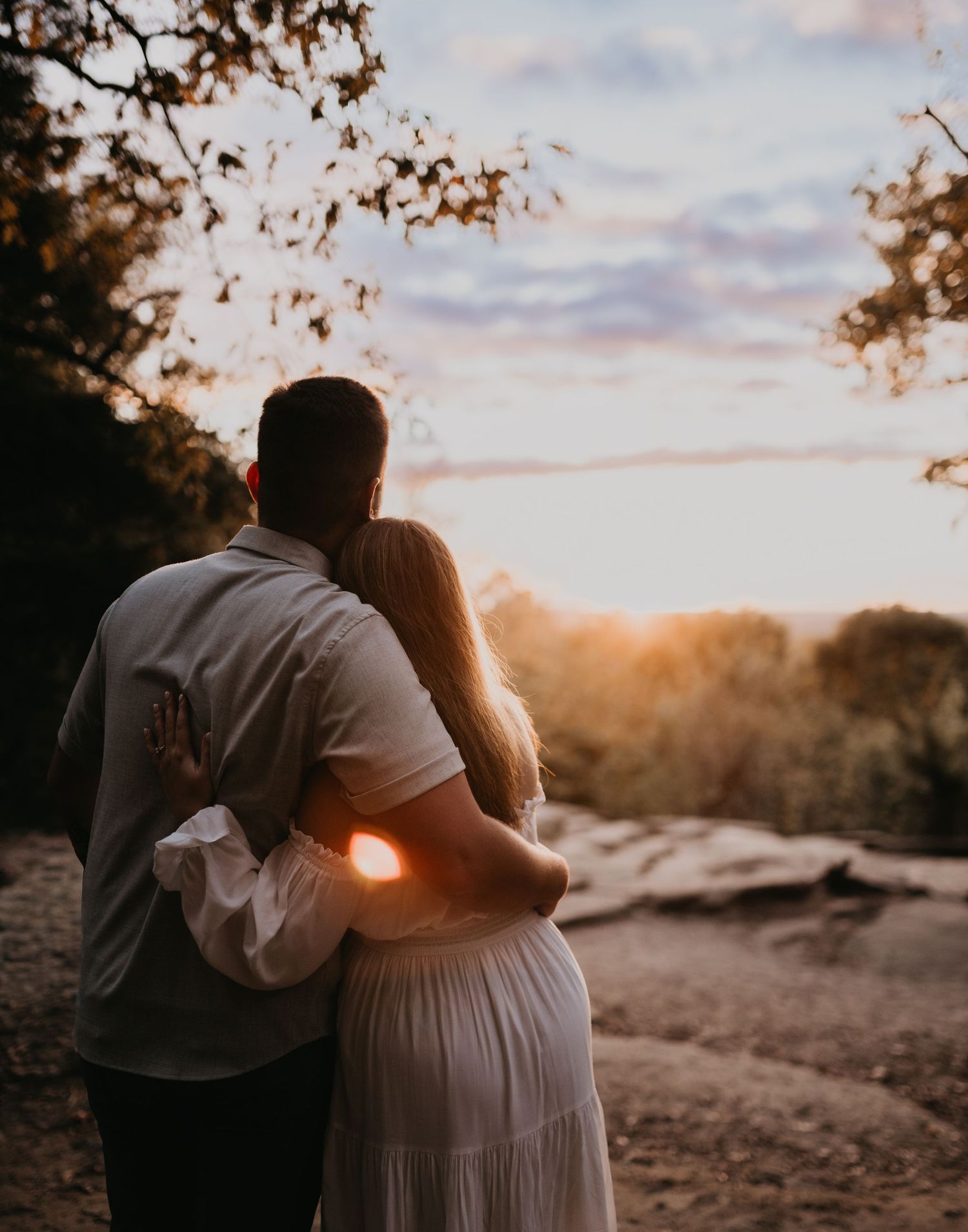 Silhouetted couple embraces against sunset sky in outdoor setting.