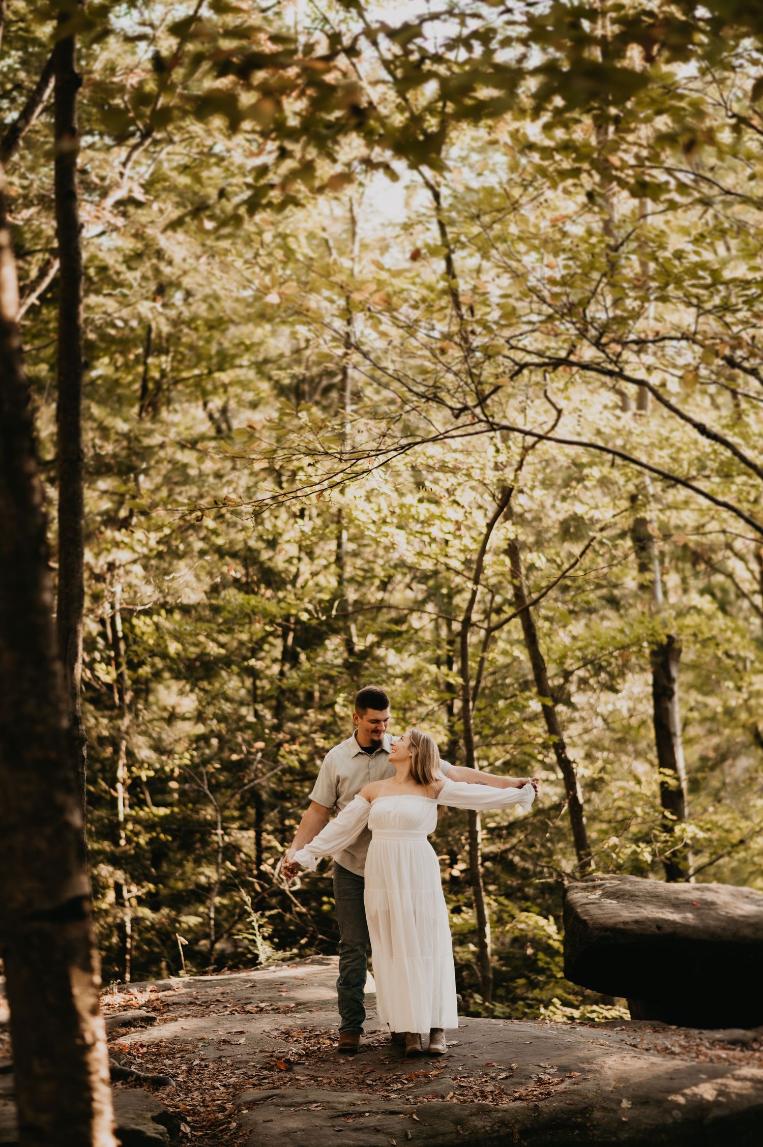 A couple shares an intimate moment in a sunlit forest setting during their outdoor wedding celebration.