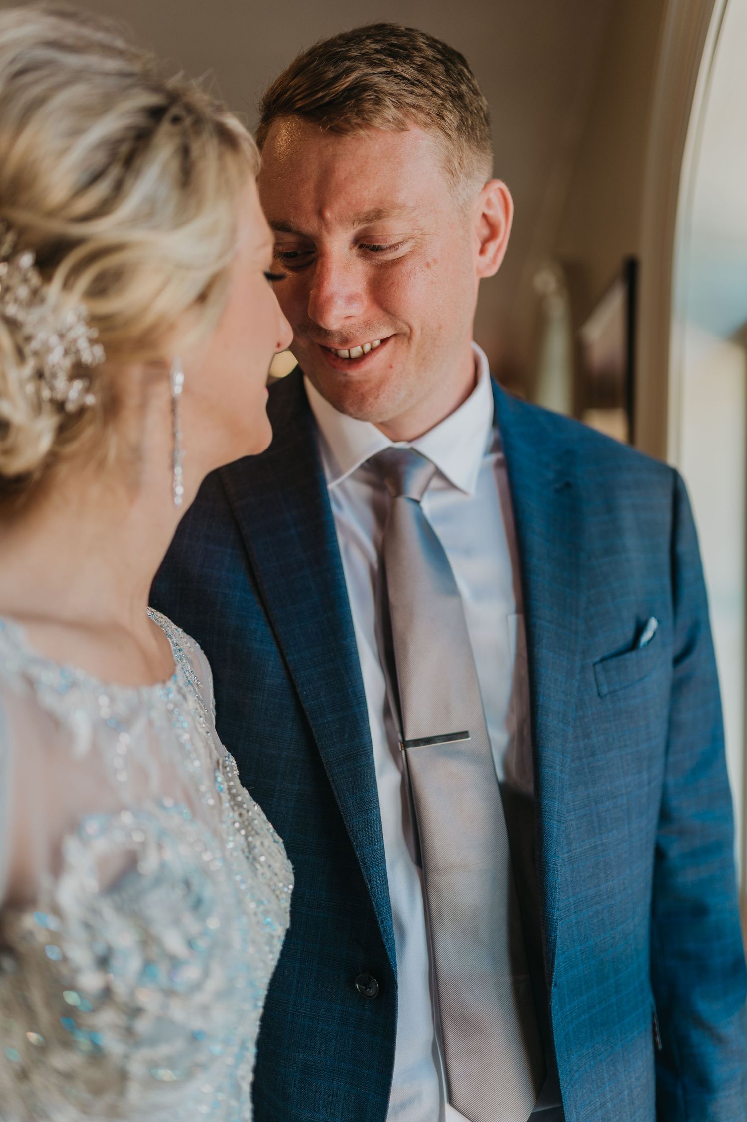 Intimate wedding moment shared between couple near a window with soft natural lighting.