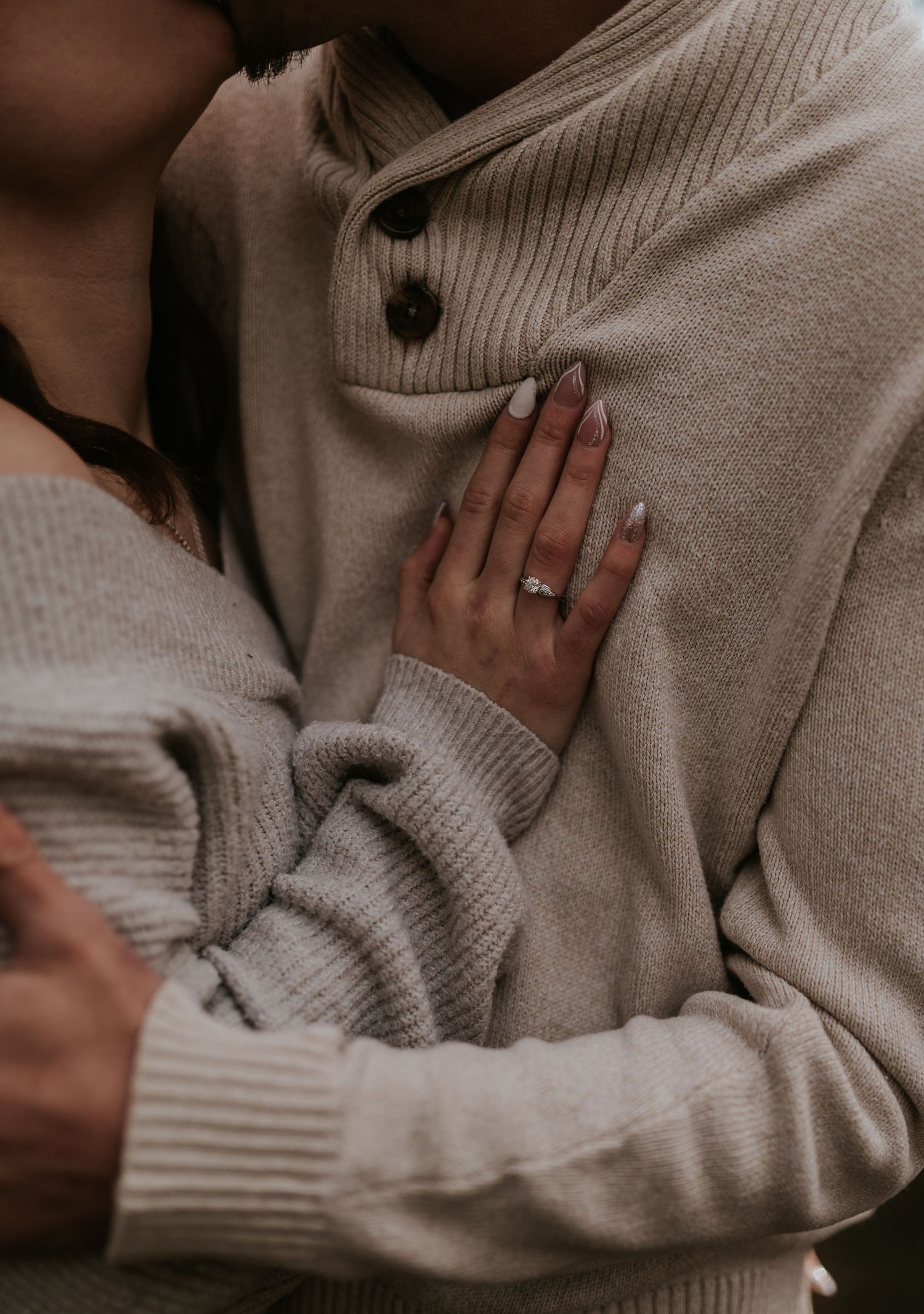Close-up of hands showing engagement ring against cream sweater.