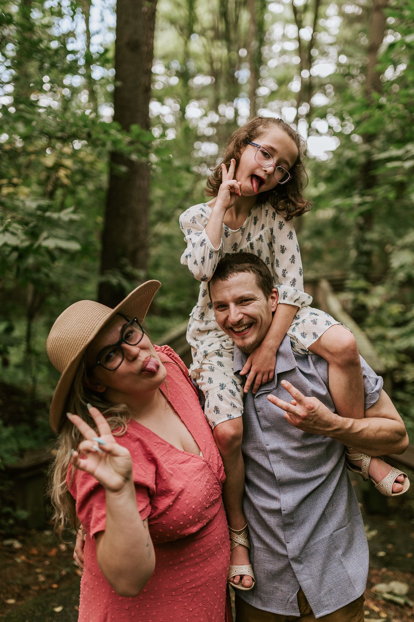A playful family portrait showing silly expressions and poses in a wooded setting.