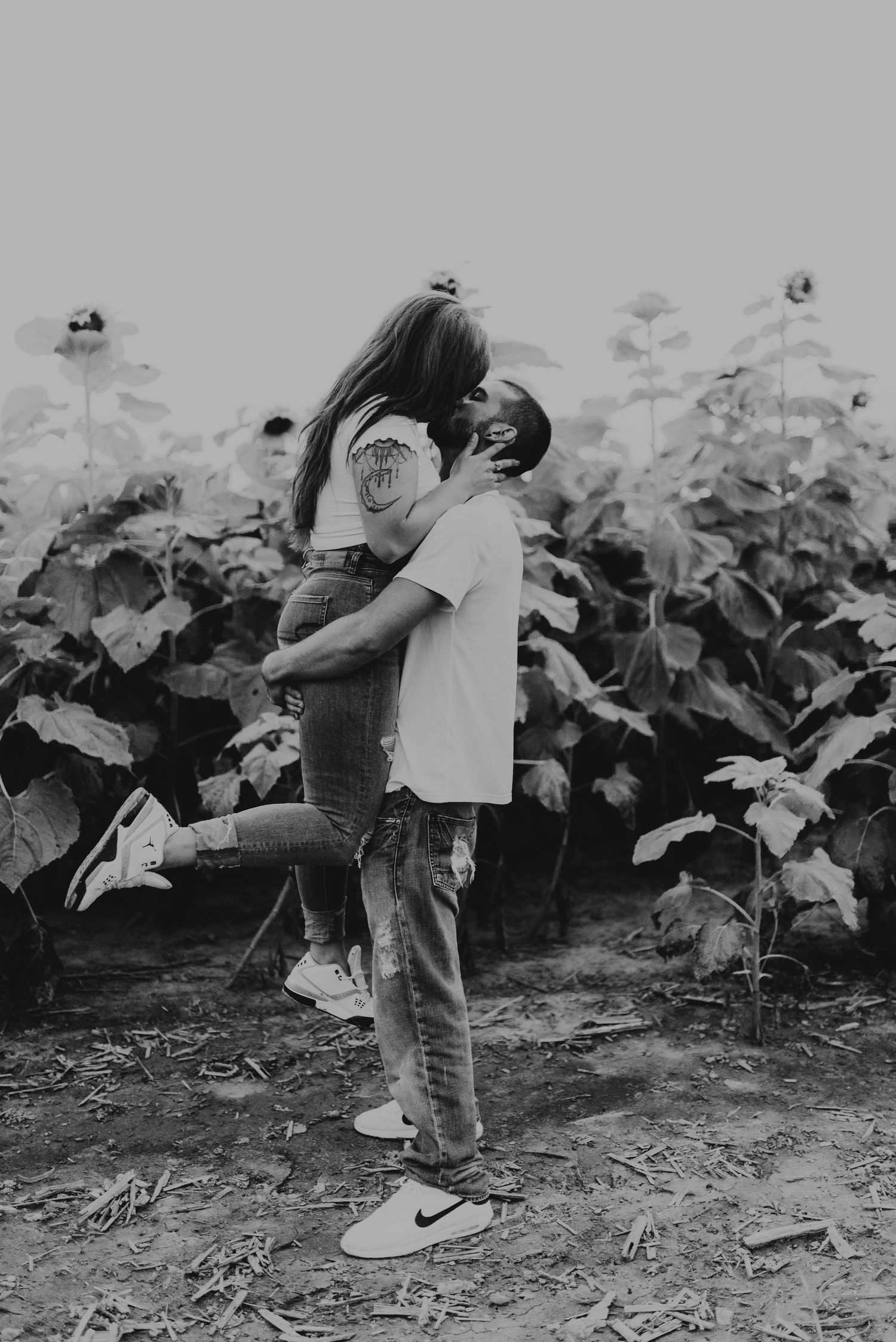 Romantic couple embracing in a field of sunflowers captured in black and white photography.