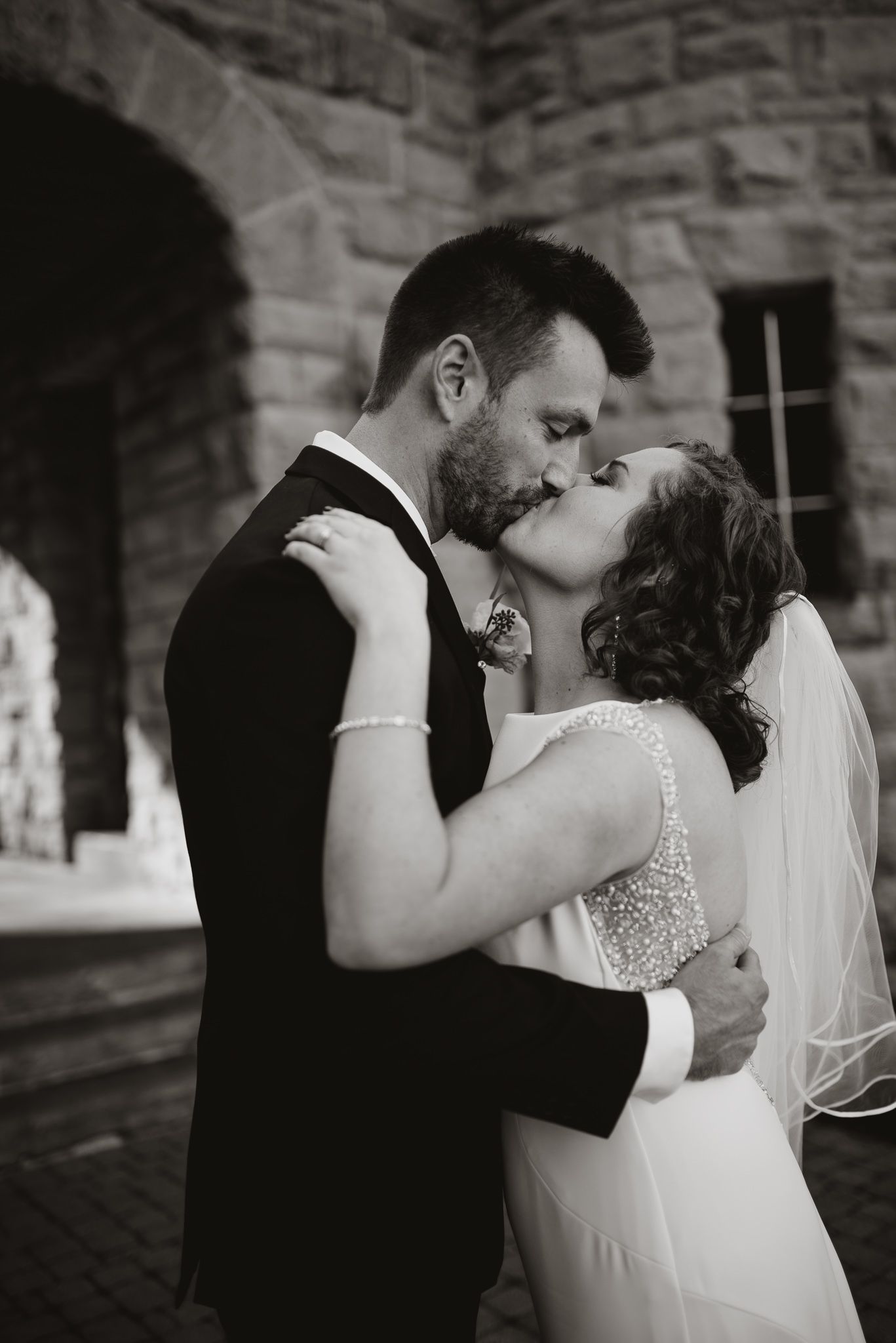 Black and white sequence of romantic wedding couple sharing intimate kisses against stone building.