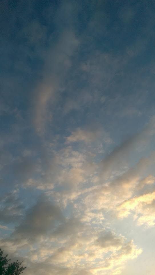 Soft blue sky with wispy clouds illuminated by warm golden sunset light, creating a serene and peaceful atmospheric scene.