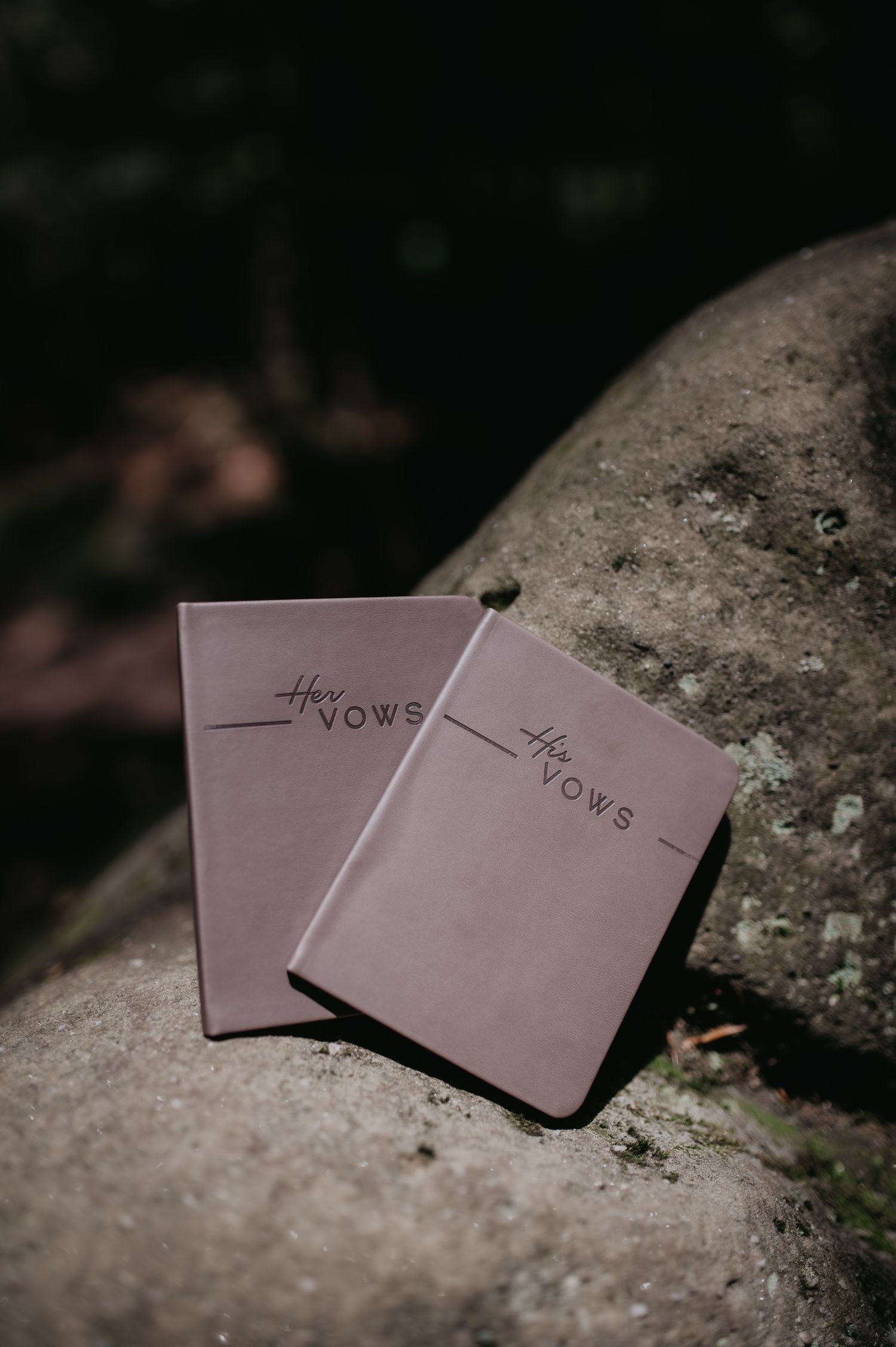 Wedding vow booklets in mauve color arranged on a textured stone surface in natural lighting.