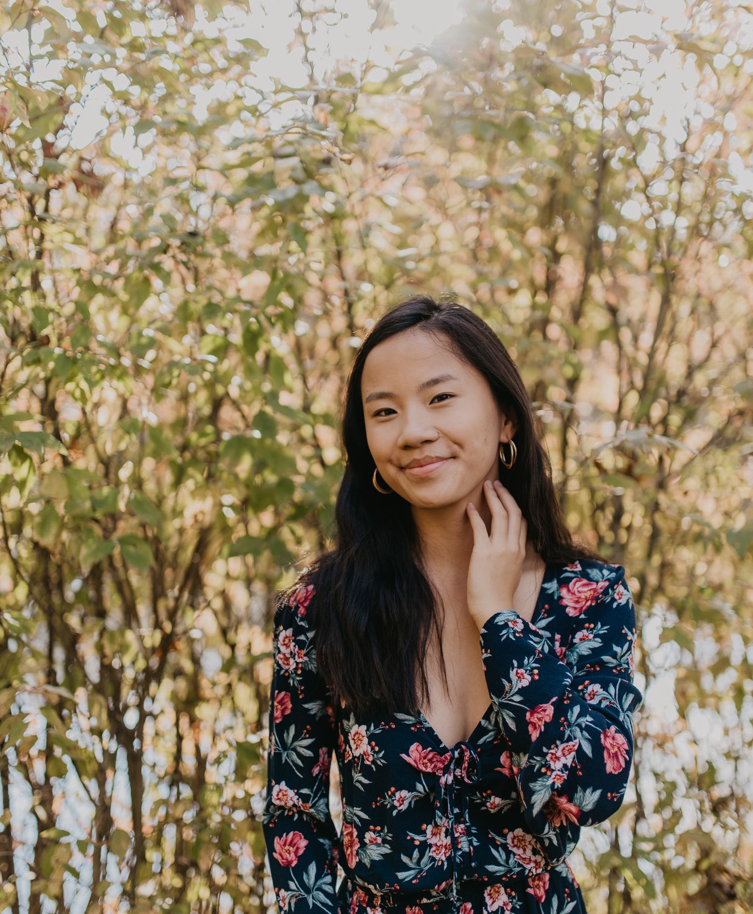 Person in floral dress smiling while posing among trees in golden light.