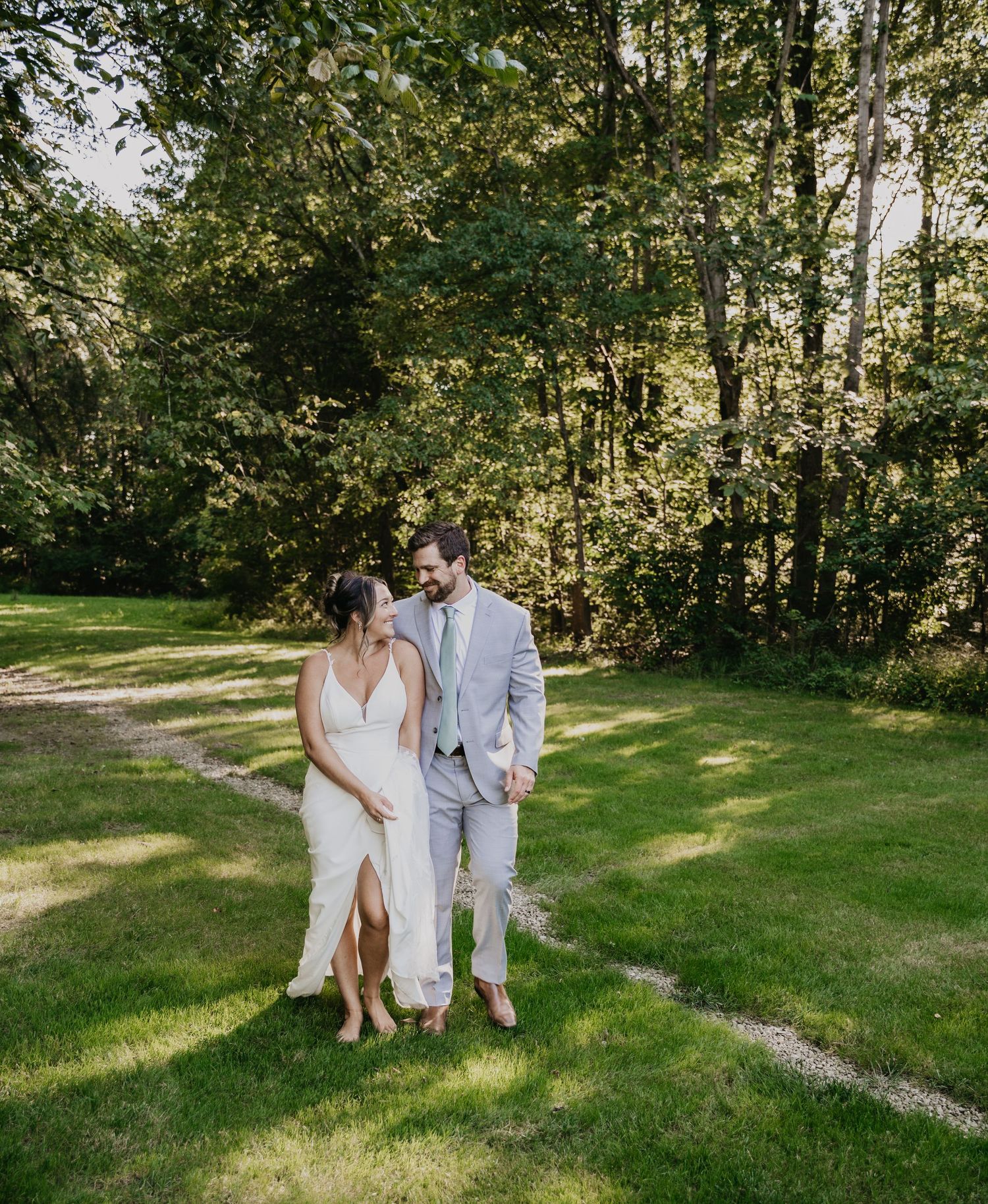 A couple in wedding attire walks along a winding path through a lush green garden setting on their special day.