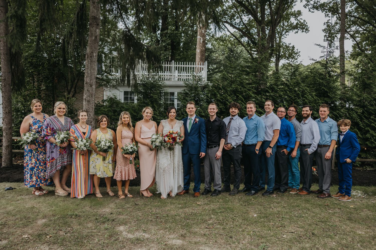 Large wedding party portrait with bridesmaids and groomsmen lined up outdoors.