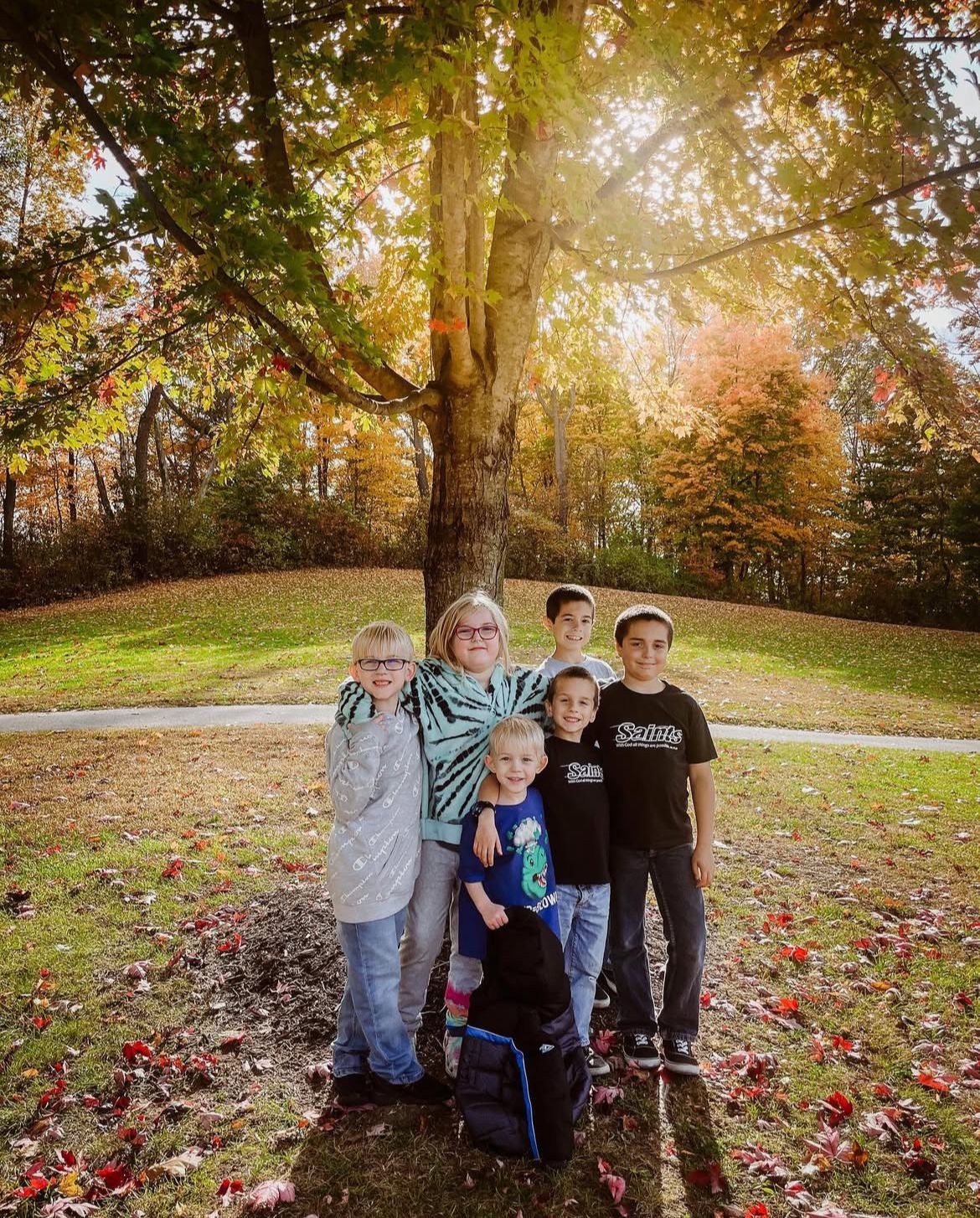 Group of children posing together under autumn trees with golden sunlight.