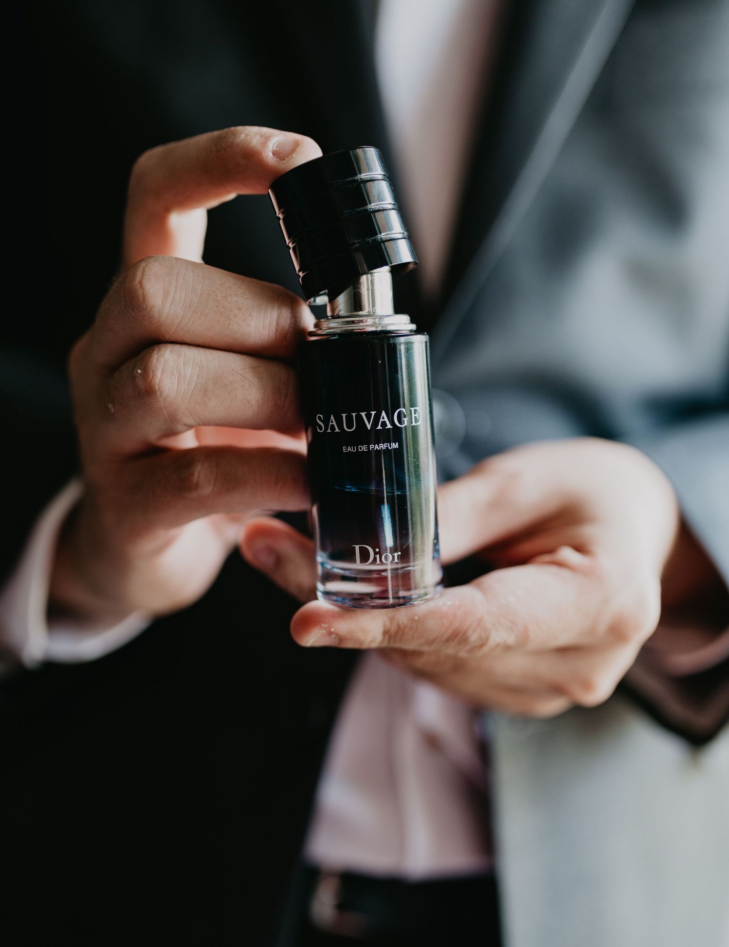 Hands holding a bottle of Dior Sauvage fragrance against a dark background.