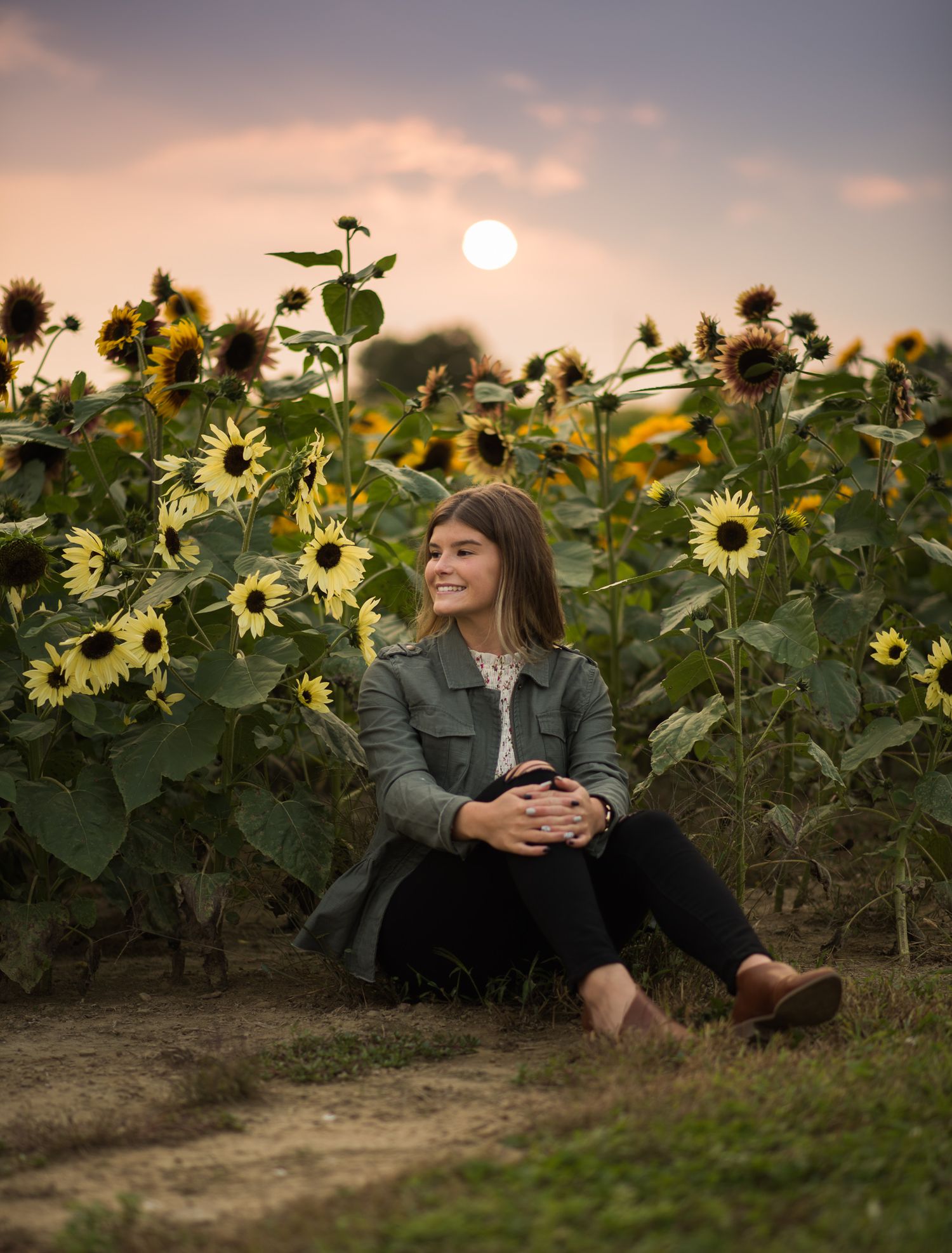 A peaceful sunset illuminates a field of tall sunflowers with a figure sitting in contemplation among the blooms.