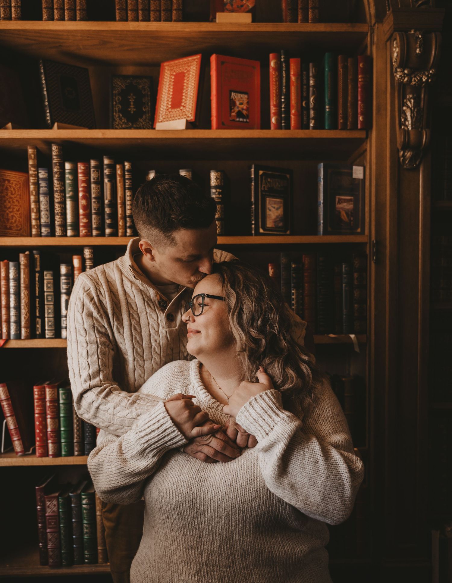 Two people share an intimate moment while standing together in a library filled with antique books and wooden shelves.