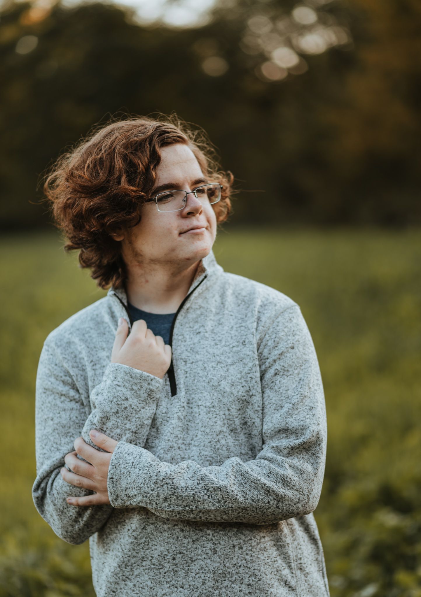 Person wearing a speckled gray sweater looks off to the side while standing outdoors in a natural setting.