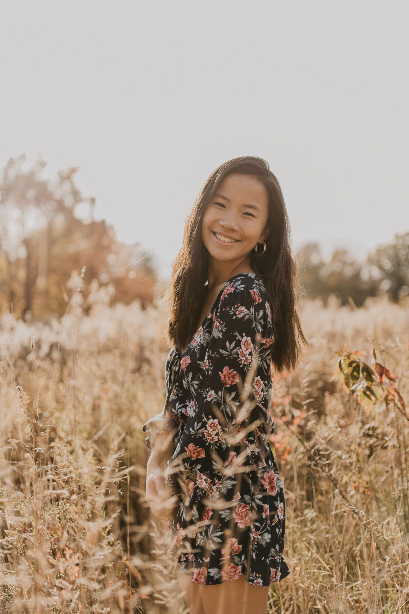 Cheerful portrait in autumn field with person wearing navy floral dress during golden hour.