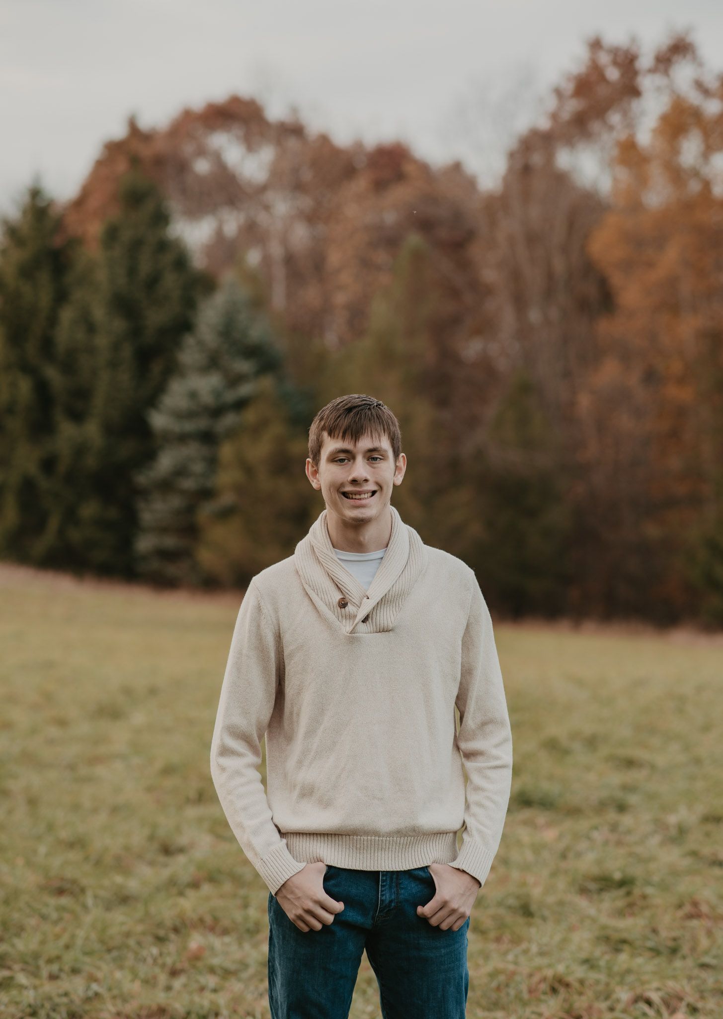 Autumn outdoor portrait in a cream shawl collar sweater against colorful trees.