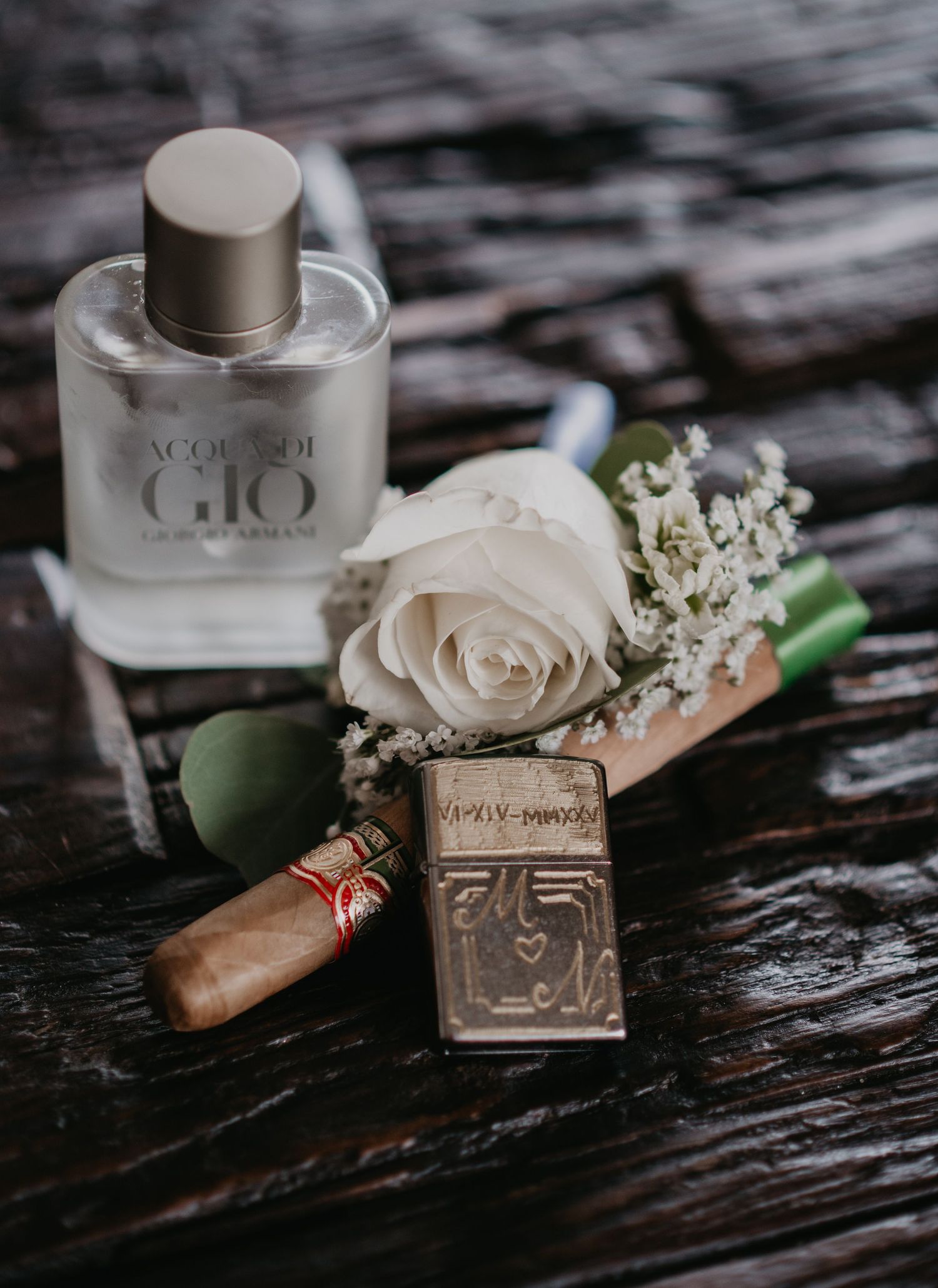 Wedding details including perfume bottles, rings, and delicate white roses arranged on dark wooden surface.