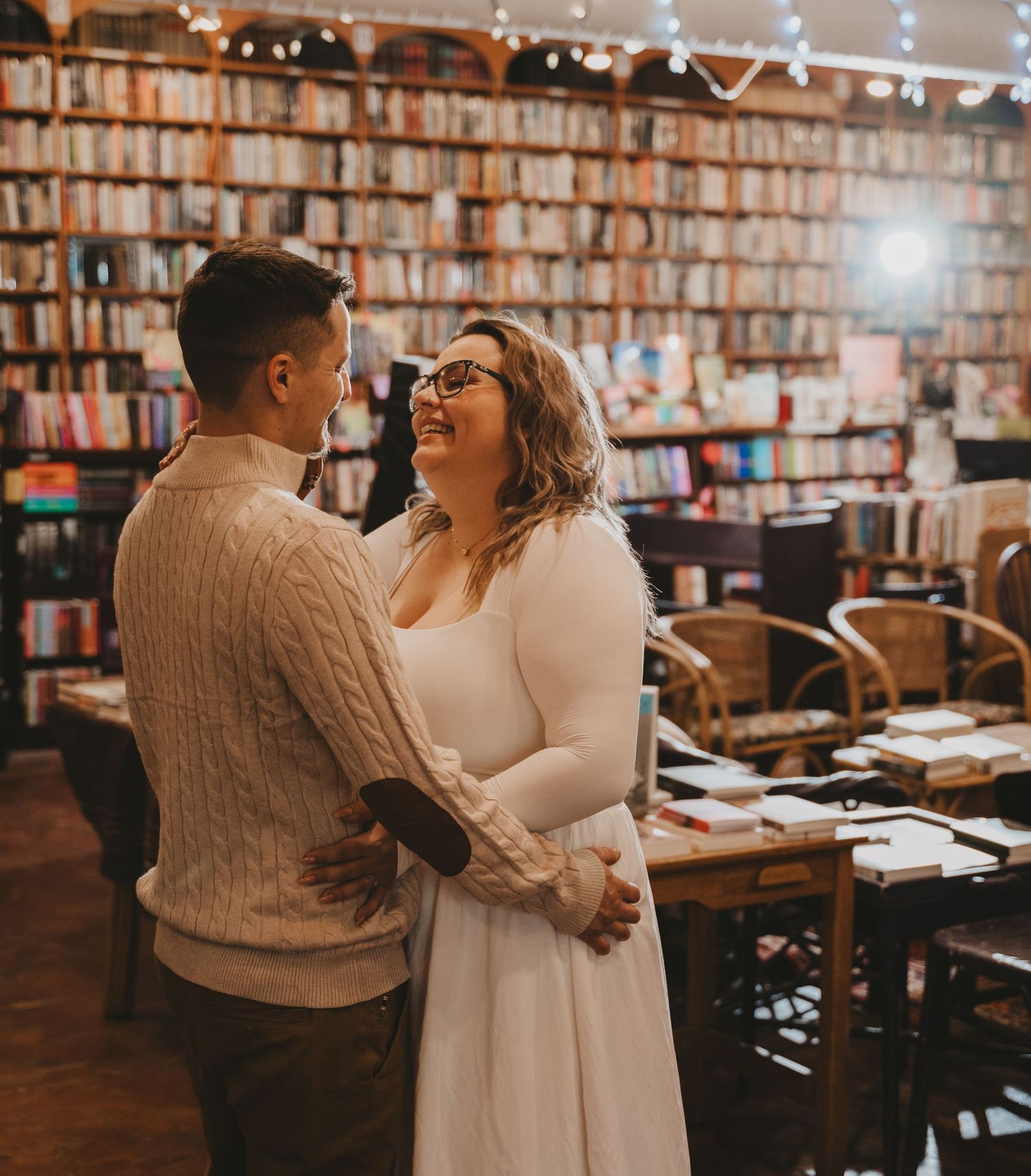 A couple shares a romantic dance moment in a cozy bookstore with wooden floors and bookshelves lining the walls.