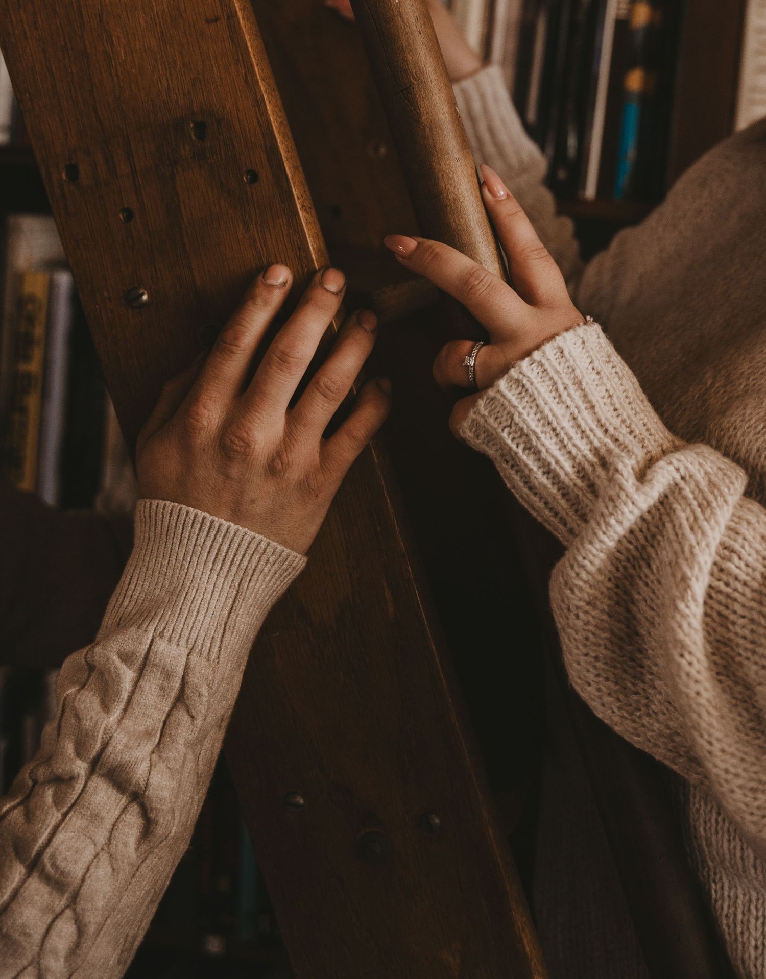 Close-up of hands wearing cozy cream knit sweaters touching a wooden surface in warm lighting.