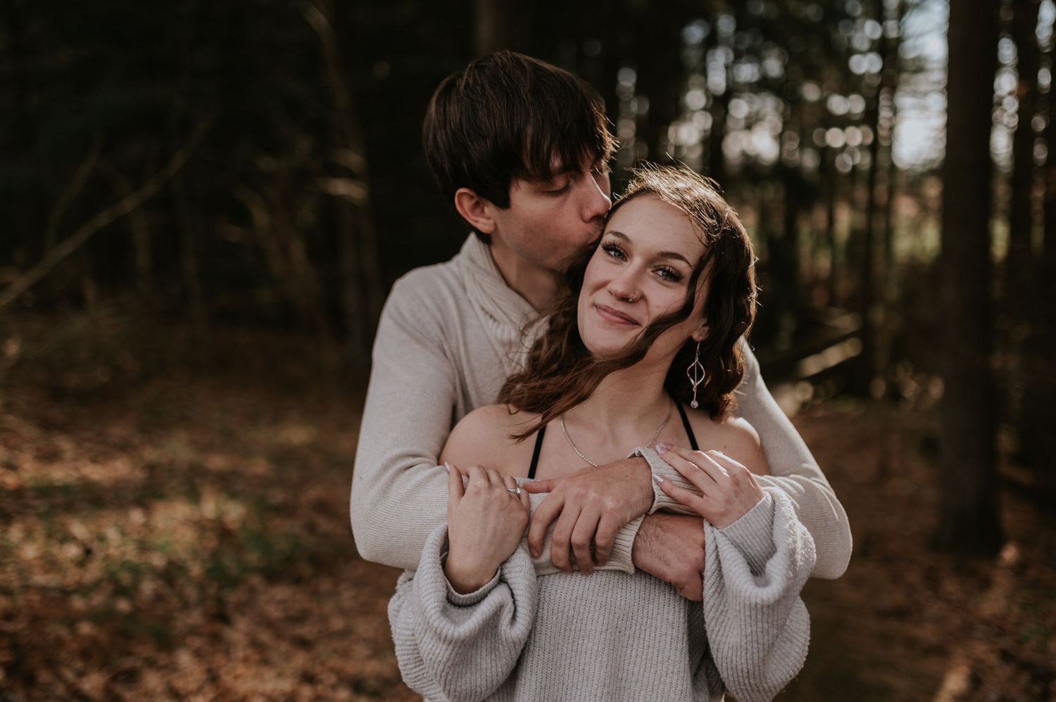 Couple in neutral sweaters sharing a tender moment among fall foliage.