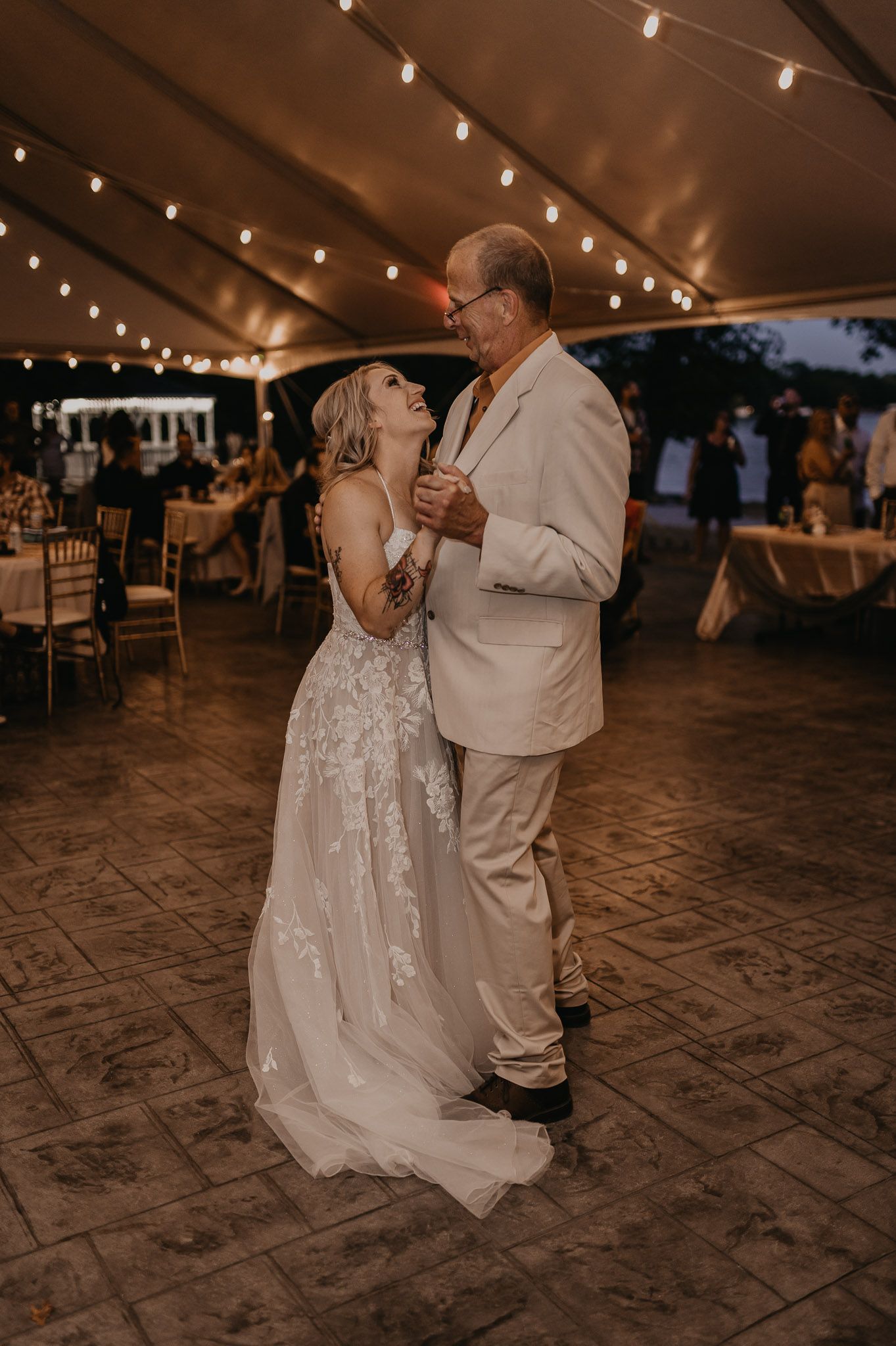 Couple shares romantic dance moment under warm reception tent lighting.