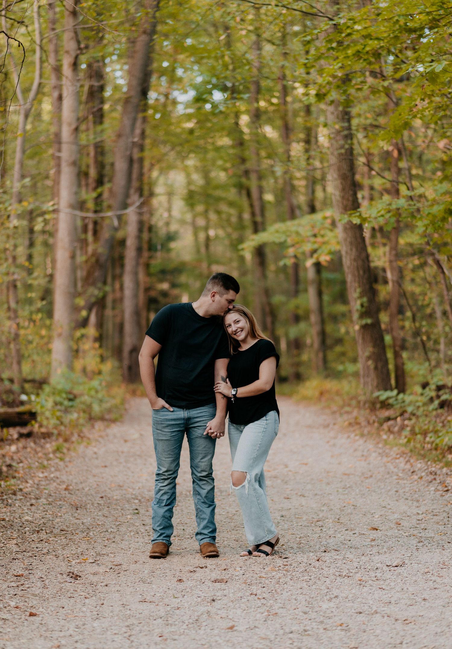 Casual couple walking and laughing together on tree-lined path in woods.