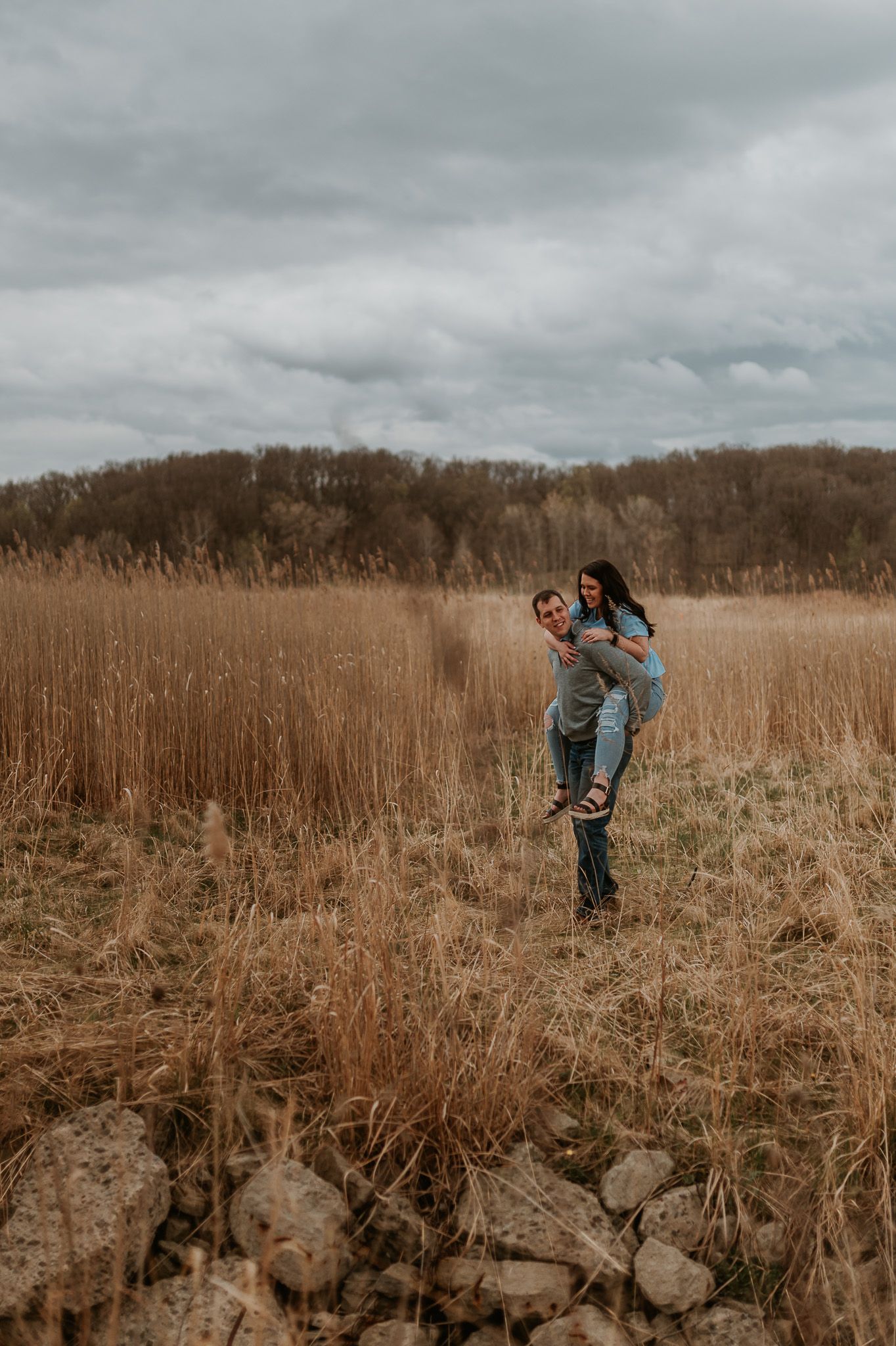 A person bends down to inspect something in a field of dried grass beneath a concrete overpass.