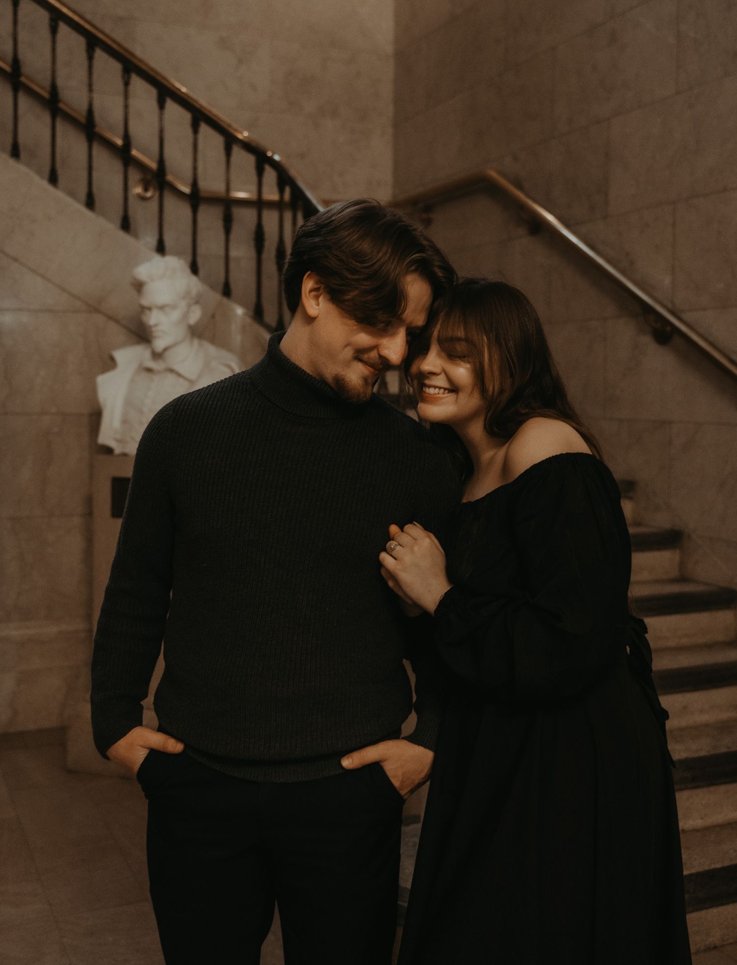 A romantic couple in black clothing embraces on a staircase in a moody sepia-toned photo series.