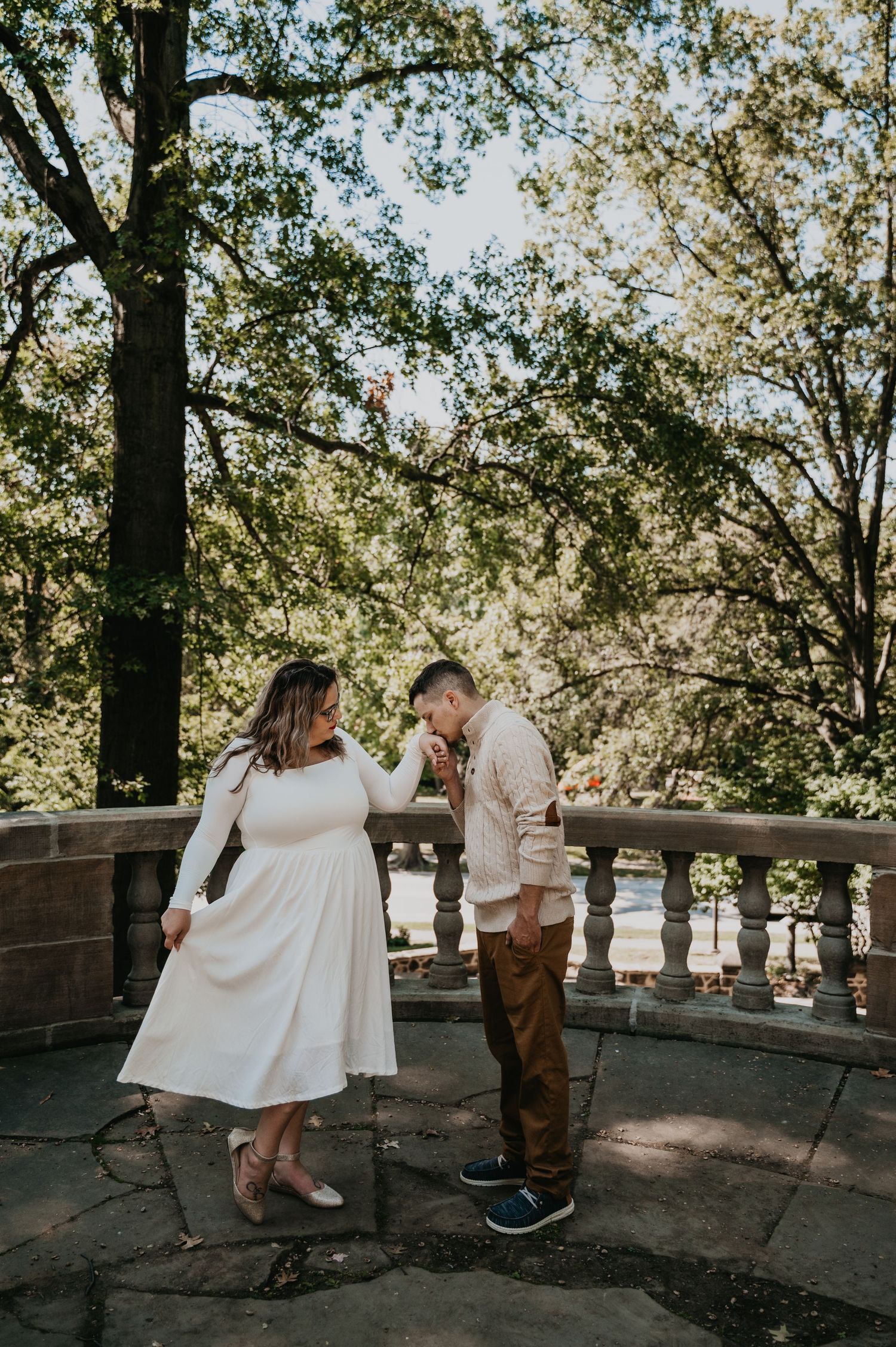 A couple shares a romantic moment on a rustic bridge surrounded by sunlit trees in a dreamy outdoor setting.