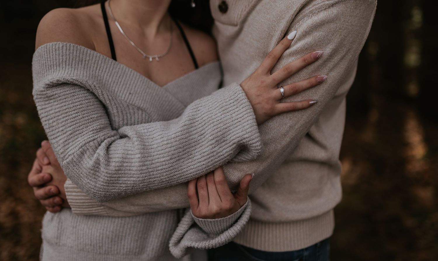 A couple wearing matching cream sweaters share tender moments during their engagement shoot.