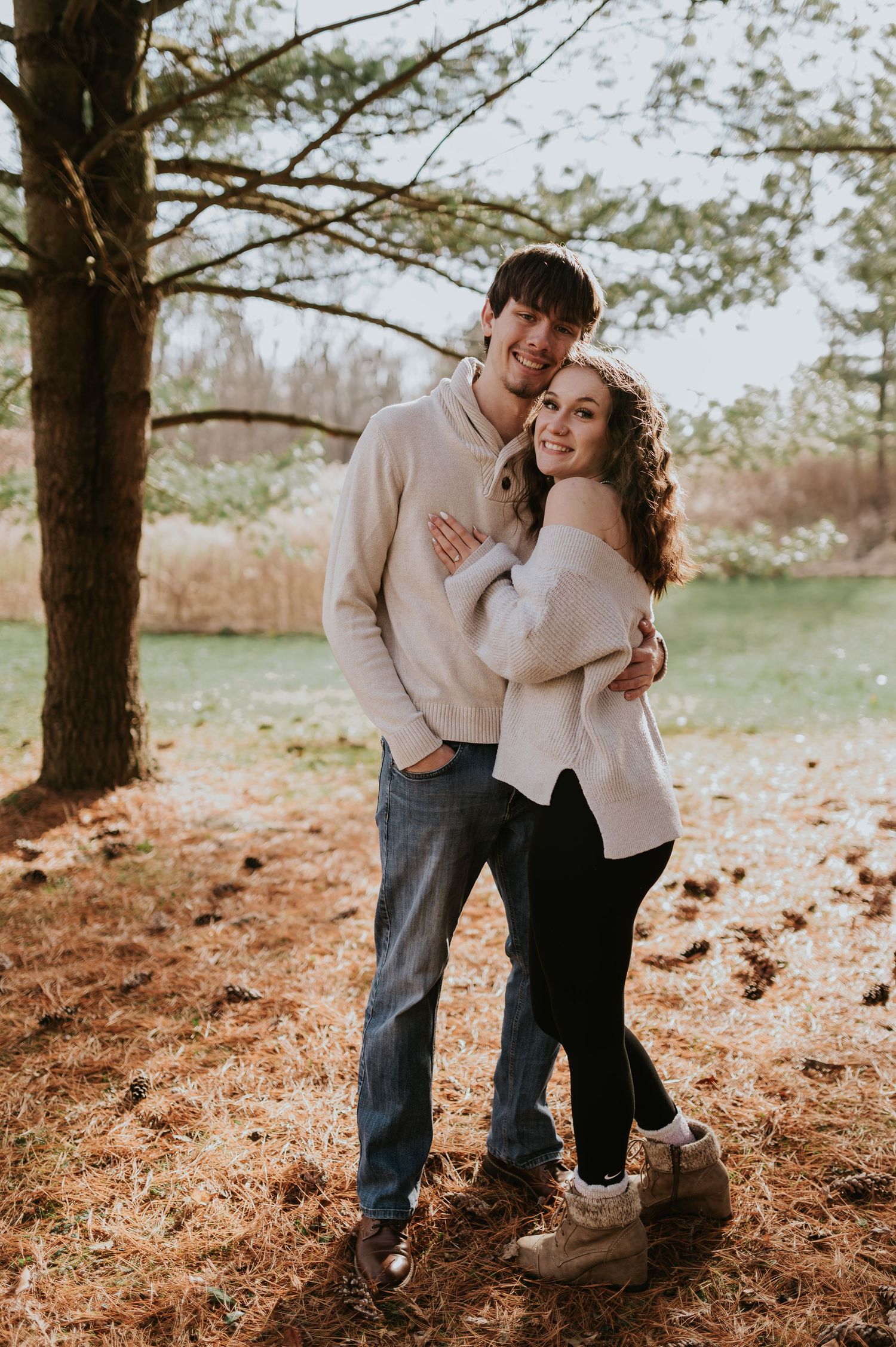 A couple in matching cream sweaters embracing outdoors during their engagement photoshoot.