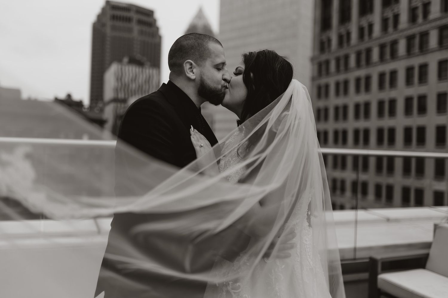 Dramatic rooftop wedding portrait with flowing veil against urban skyline.
