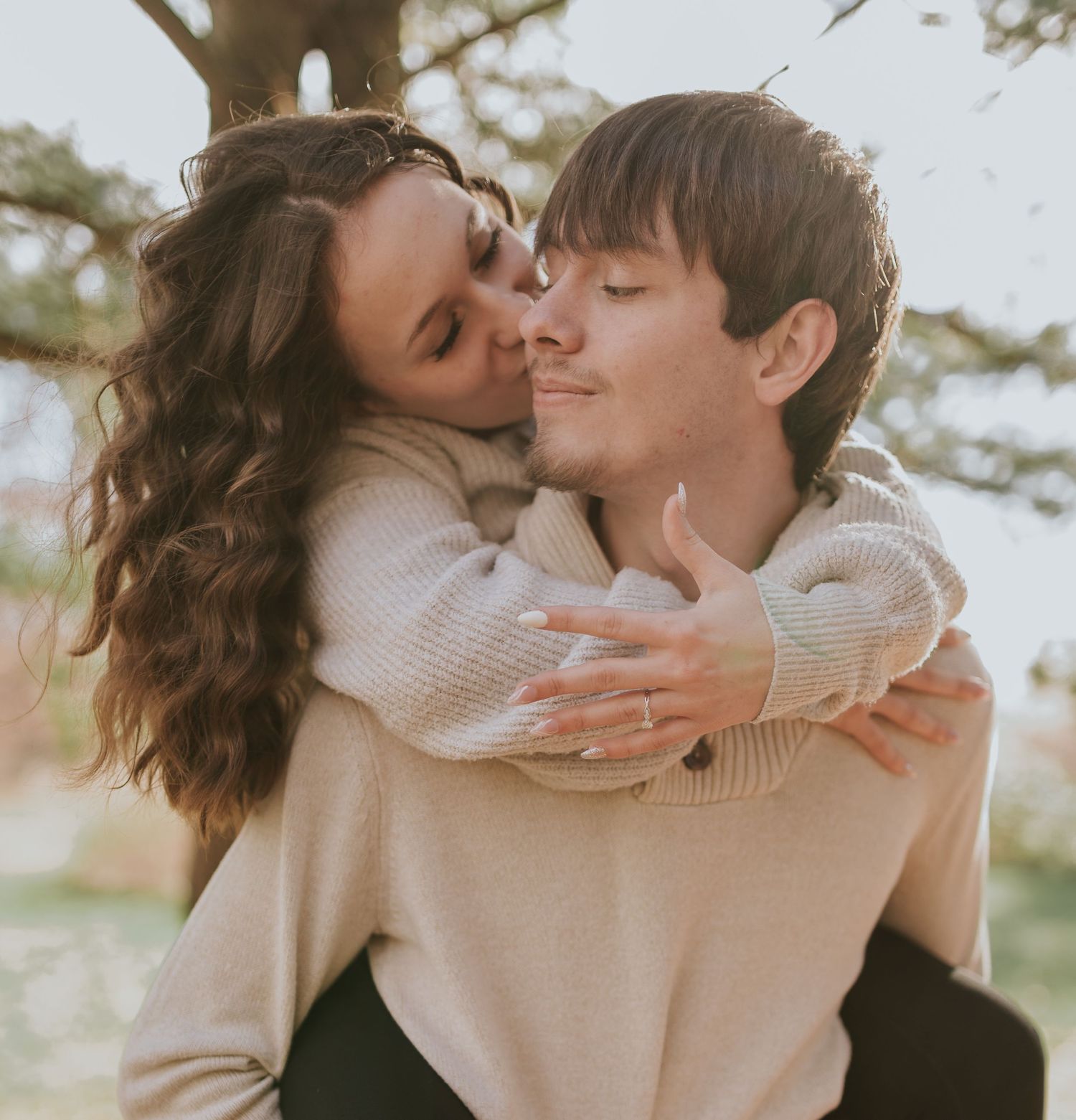 Couple sharing an intimate piggyback kiss in warm sunlit forest setting.
