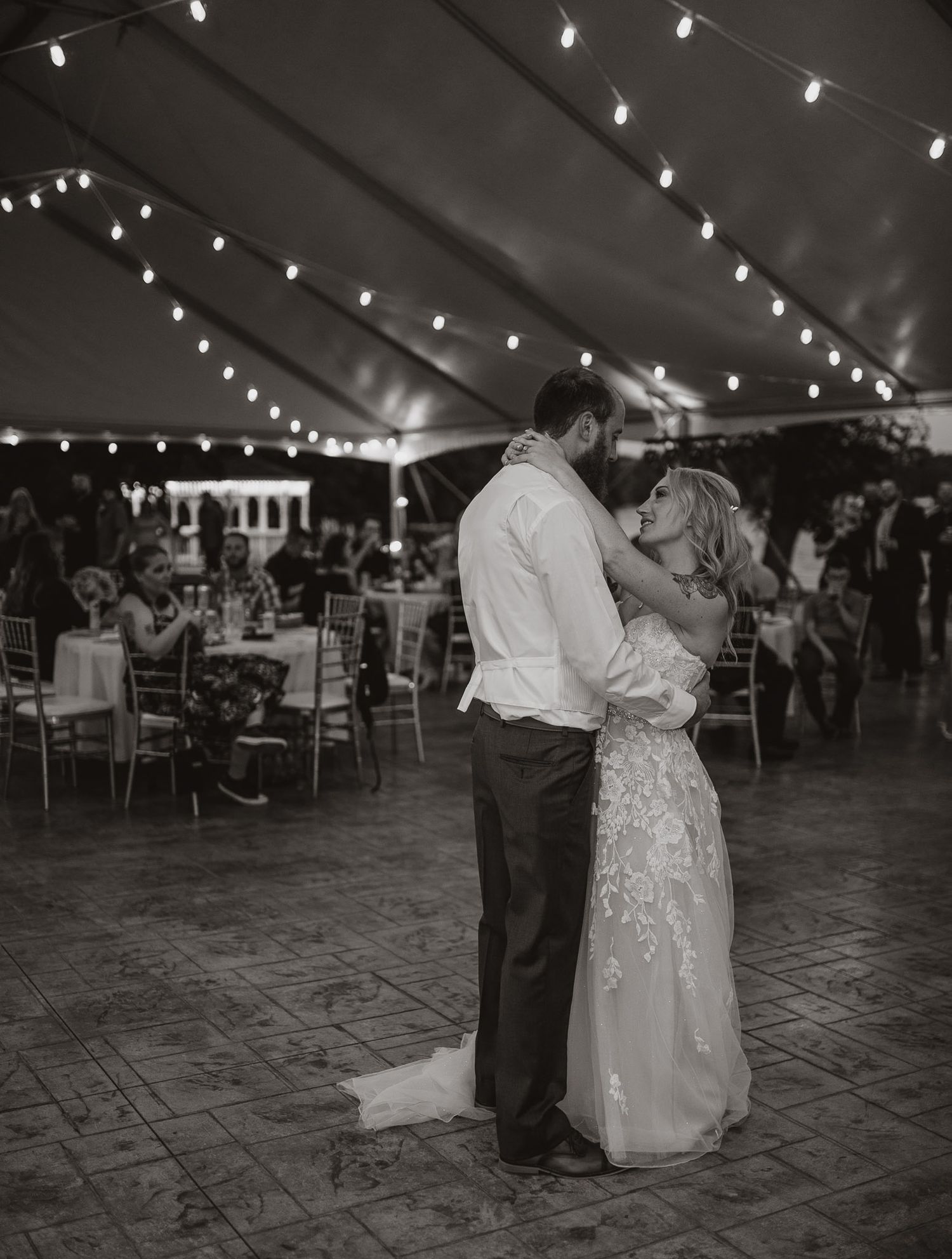 Wedding couple shares first dance under twinkling lights in reception tent.