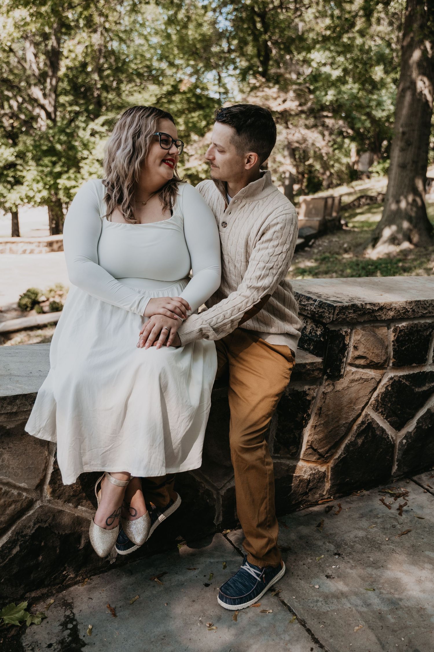 A couple sits together on rustic wooden steps in a sunlit outdoor setting, sharing intimate moments in casual attire.