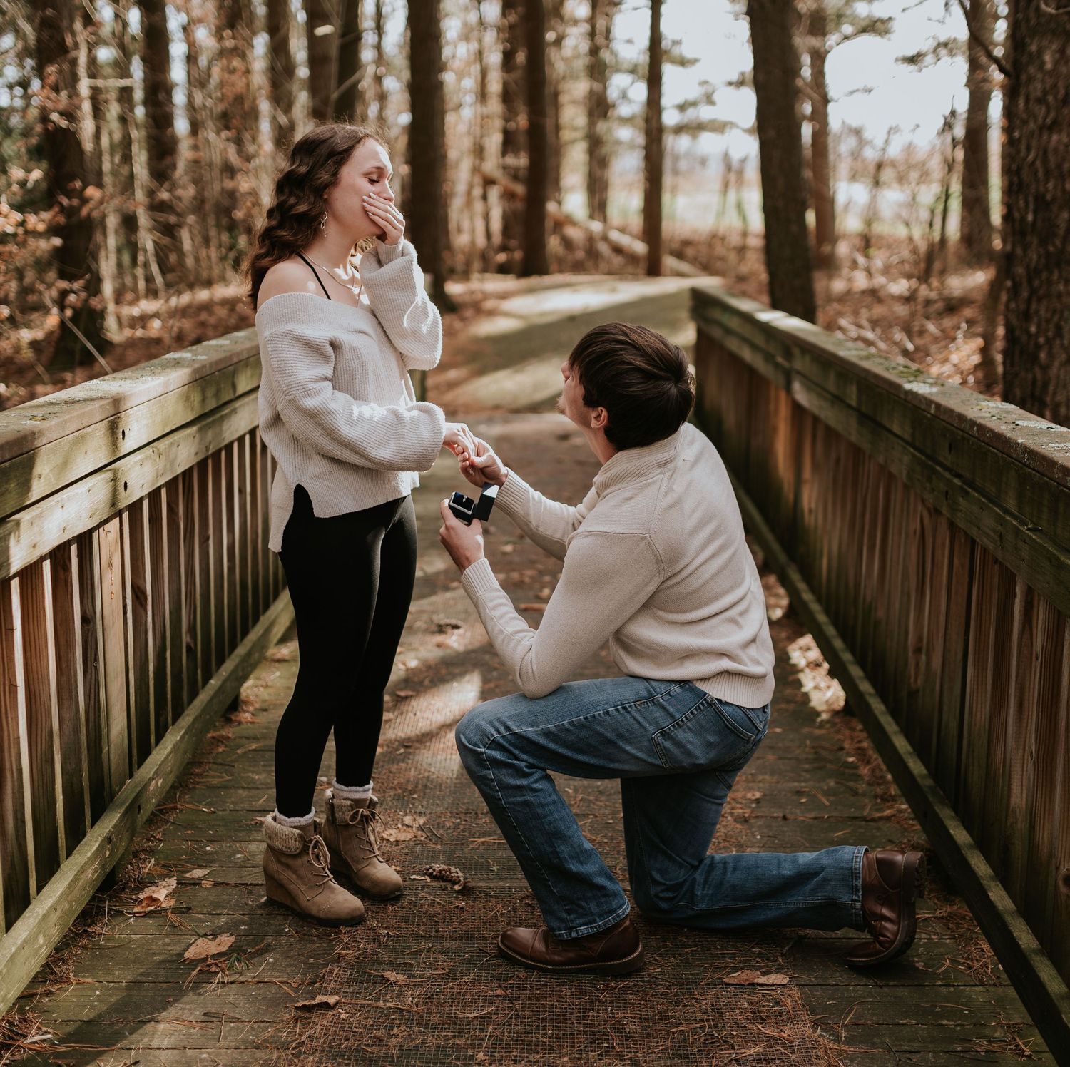 A surprise proposal photographed on a rustic wooden boardwalk surrounded by autumn trees.