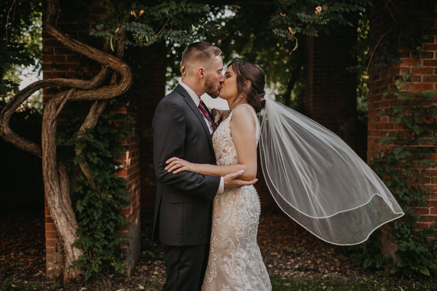 Intimate wedding portraits in front of rustic brick wall with vines and natural lighting.