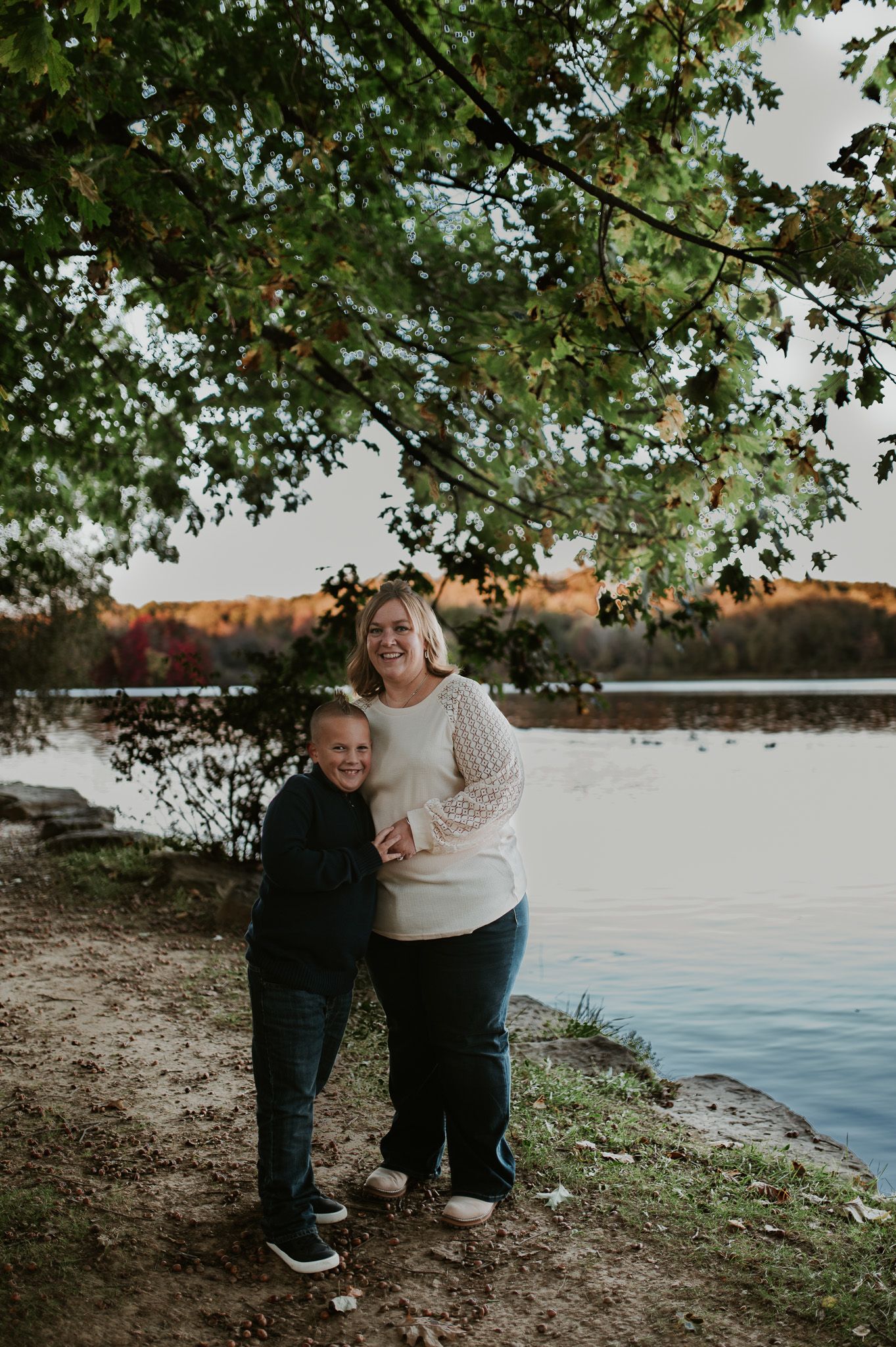 Two figures share a warm embrace while standing by a scenic lake at sunset.