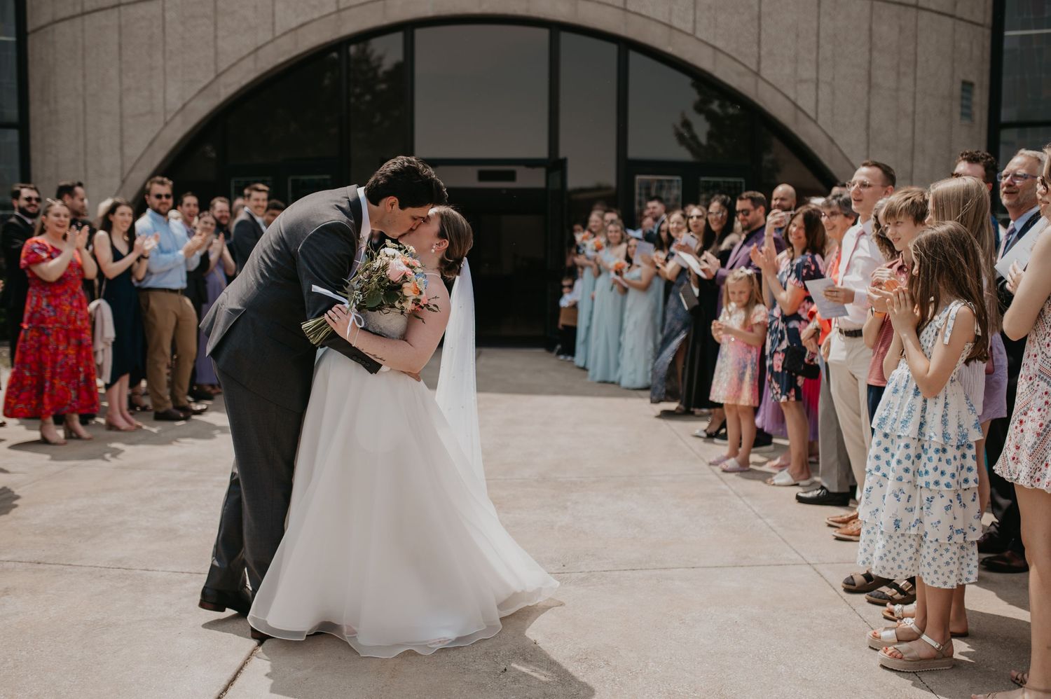 A couple shares their first dance outside a church while wedding guests line up on both sides to celebrate.