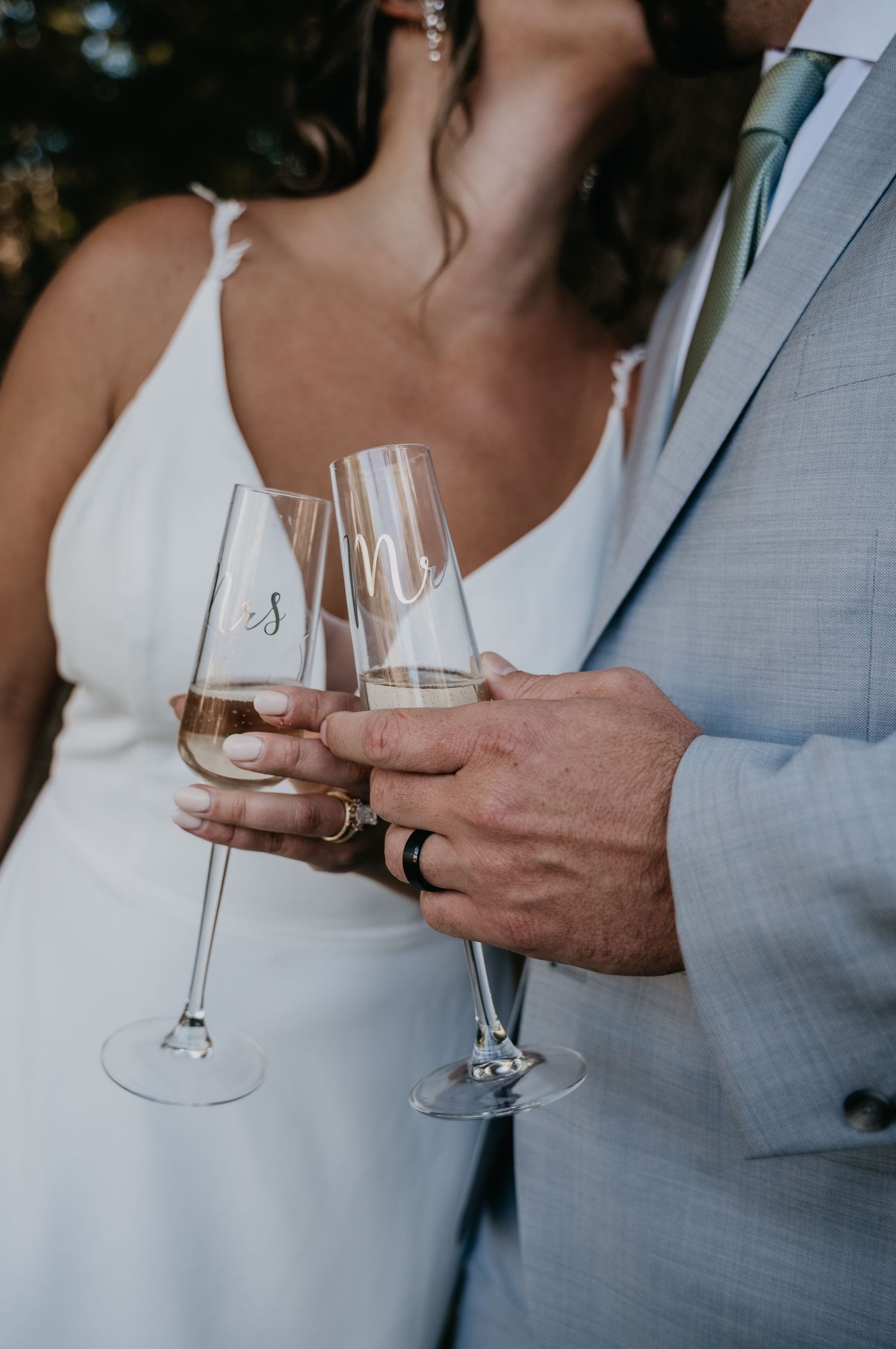 Close-up of wedding couple holding wine glasses in elegant attire during a toast celebration.