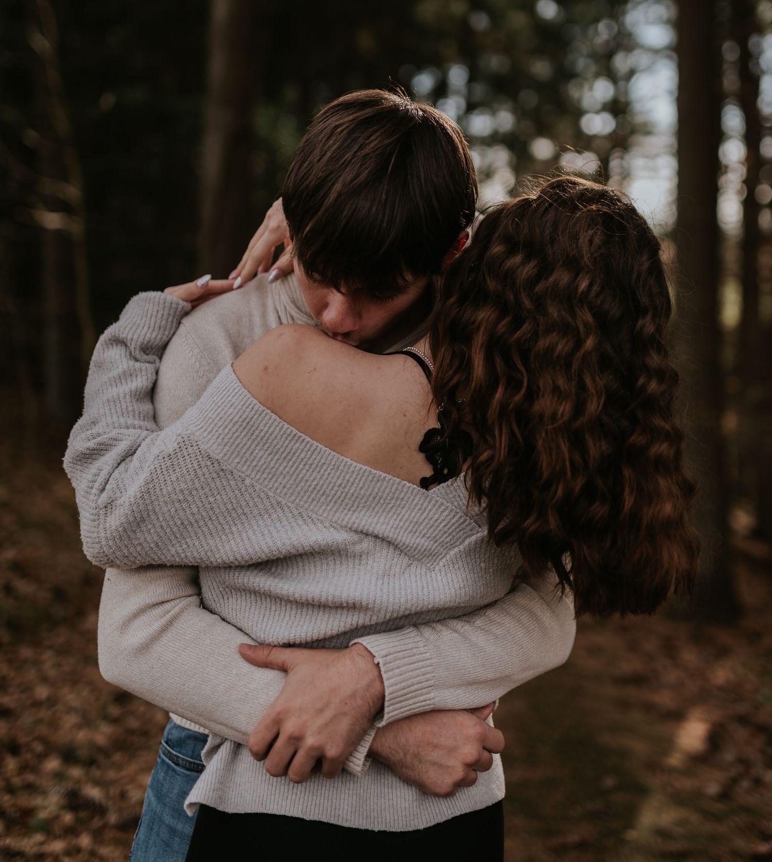 Intimate embrace between couple wearing matching sweaters in a wooded setting.