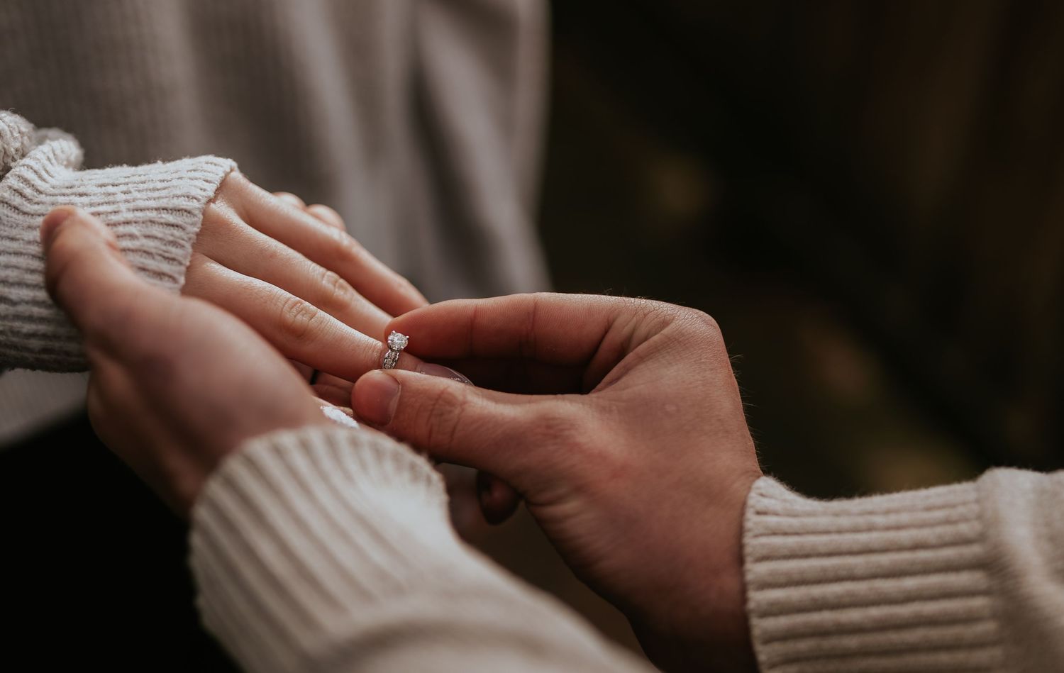 Intimate close-up of hands during a ring exchange wearing cozy sweaters.