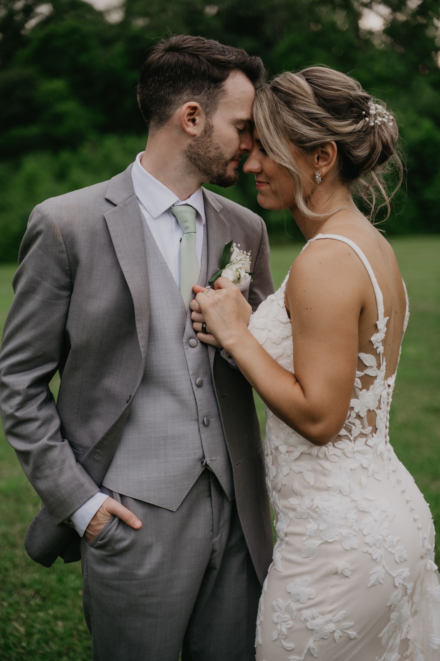 A romantic wedding couple shares intimate moments in a garden setting wearing grey suit and lace dress.