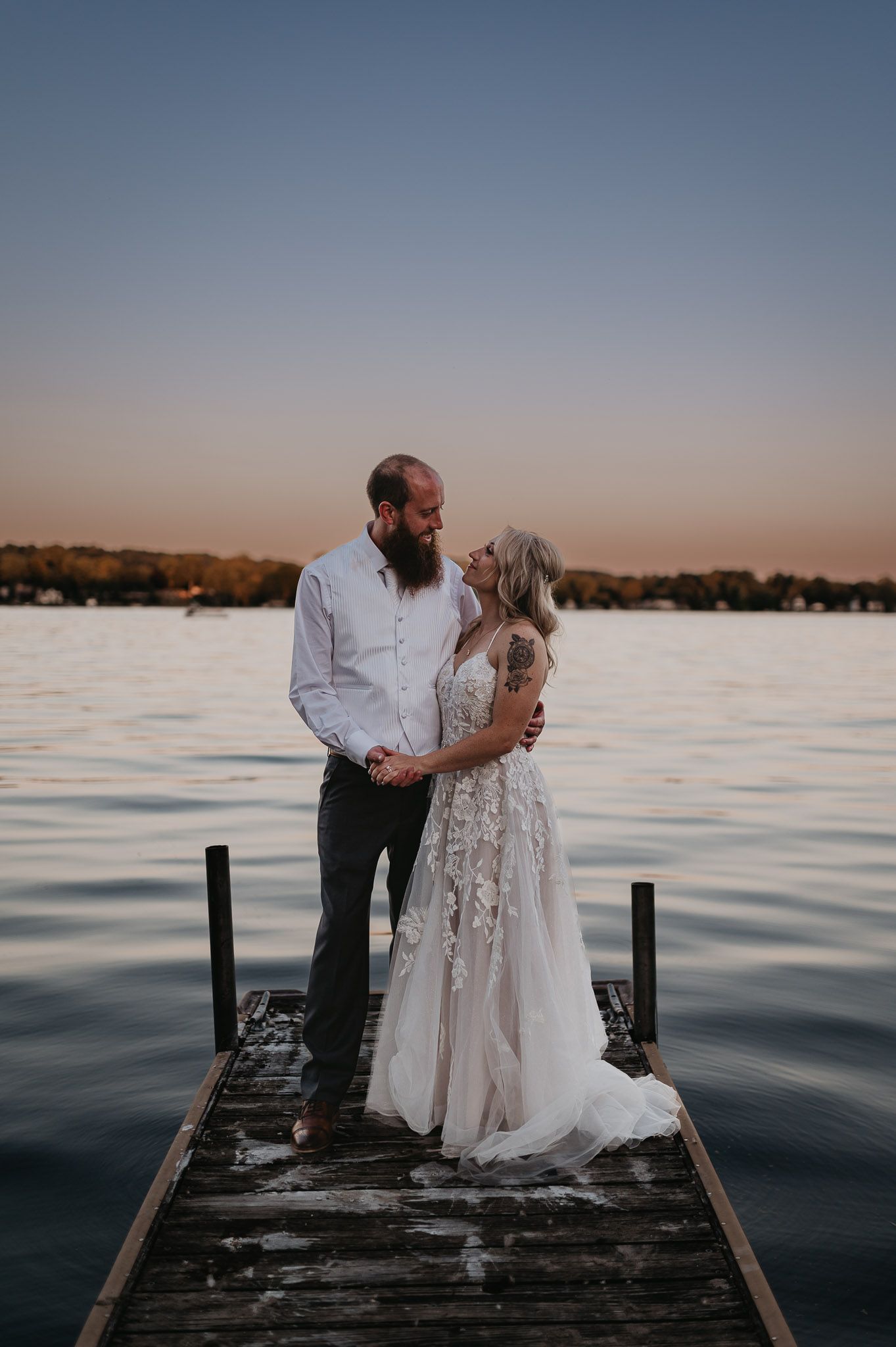 A couple shares an intimate moment on a wooden dock during sunset over a serene lake.