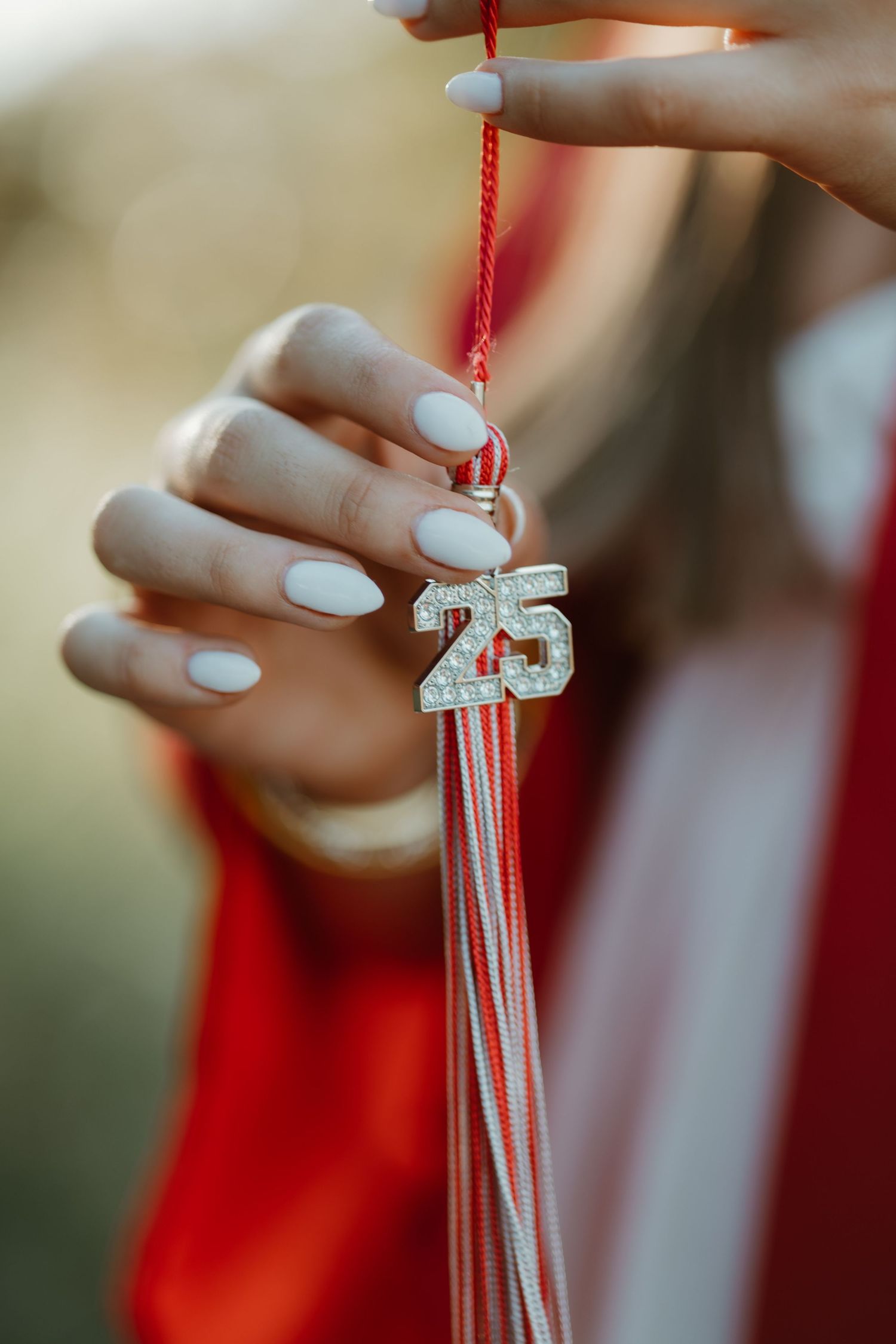 Close-up view of hands with white manicured nails manipulating delicate white silk knots against a red background.