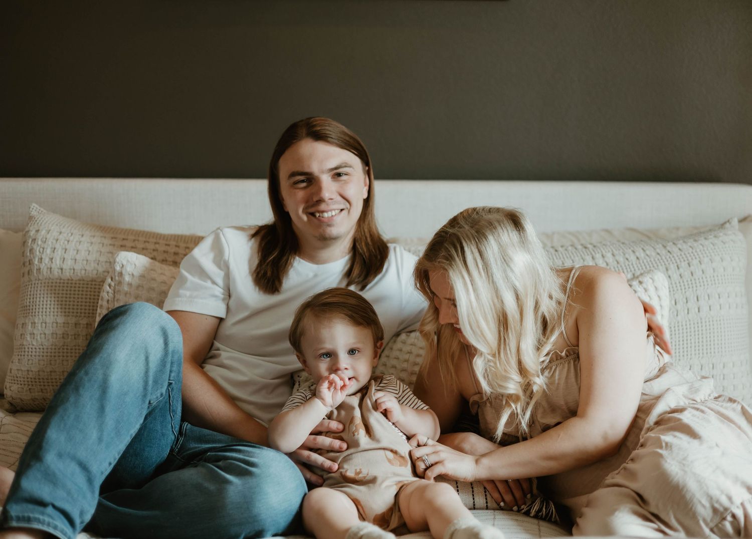 Parents lovingly cuddle with their sleeping baby in bed during an intimate family lifestyle photoshoot.