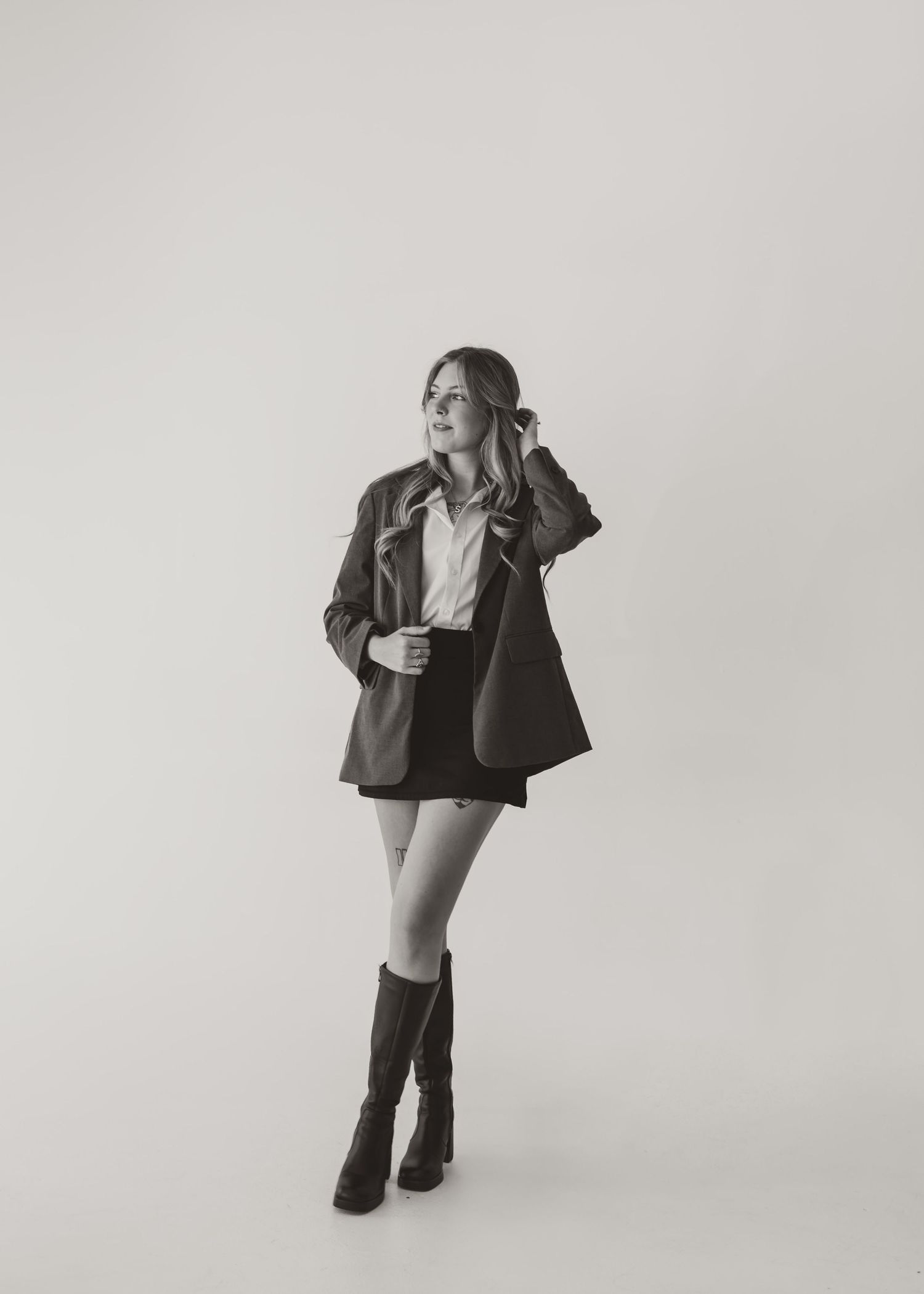 Black and white fashion photo showing a stylish outfit with blazer, shorts and knee-high boots against white backdrop.
