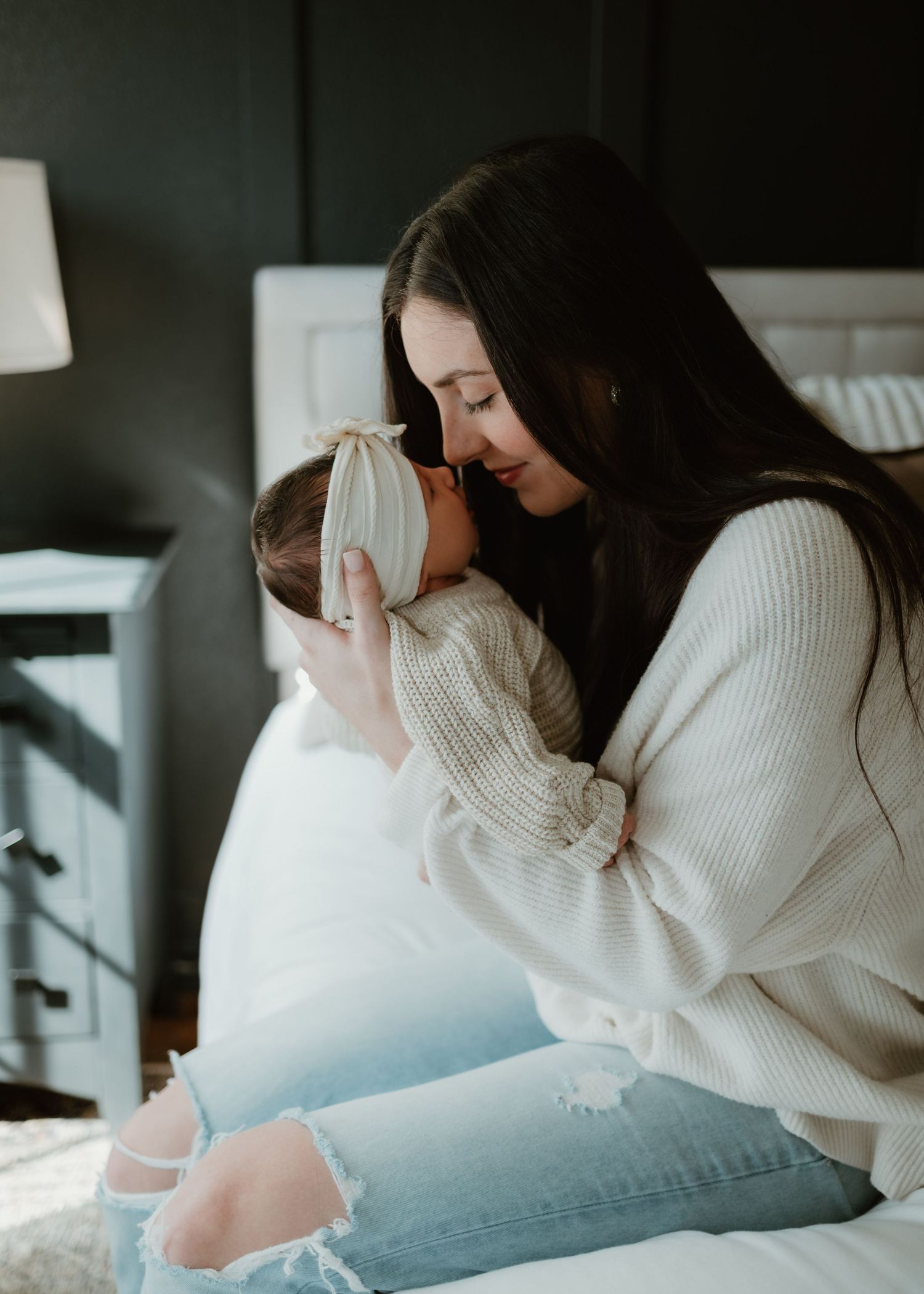 Woman in cream sweater reclines on gray couch while gazing downward in subdued lighting.